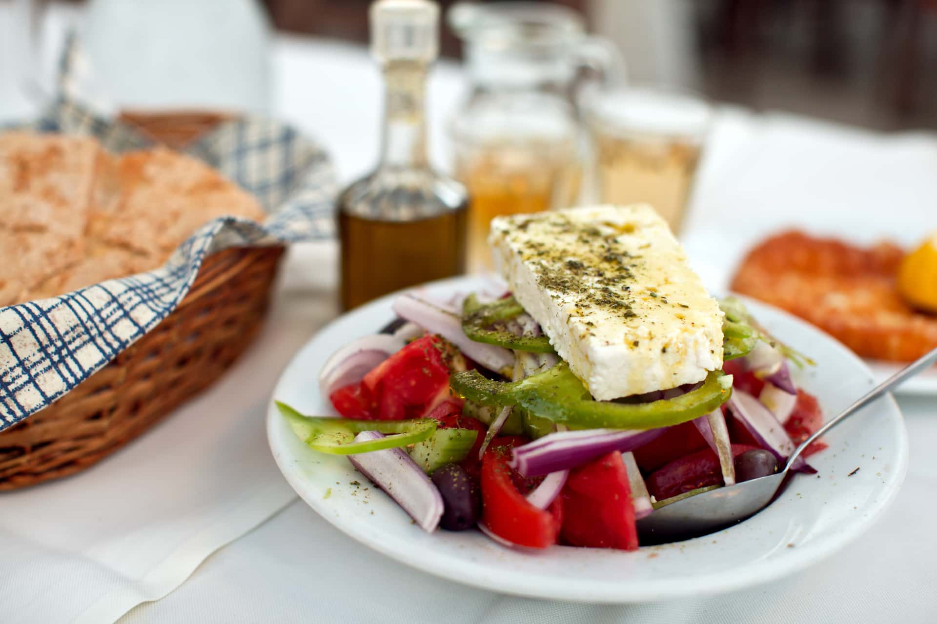 Greek salad with feta cheese, tomatoes, and olives served outdoors with bread and drinks.