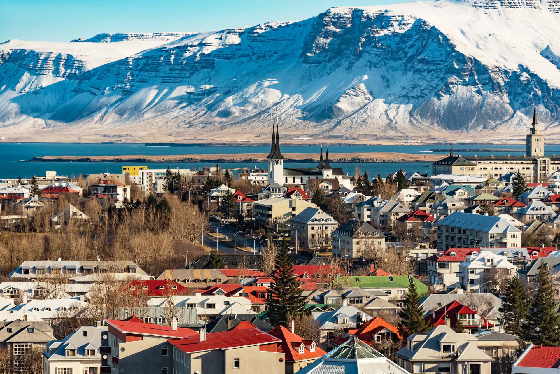 City of Reykjavik with colorful roofs, church spires, and snow-capped mountains across the water.