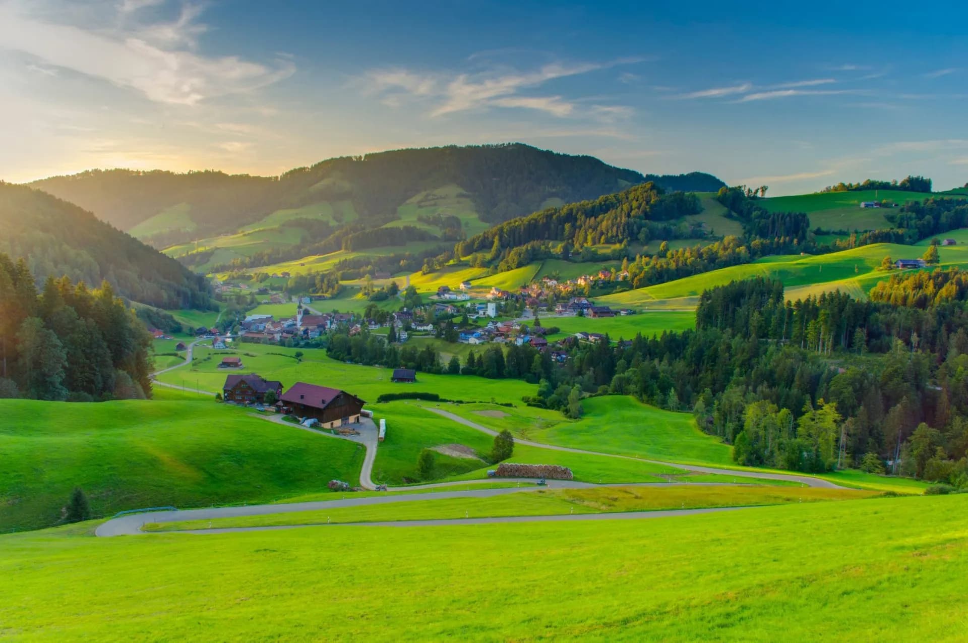 Lush green Swiss countryside valley with a small village nestled among rolling hills at sunset