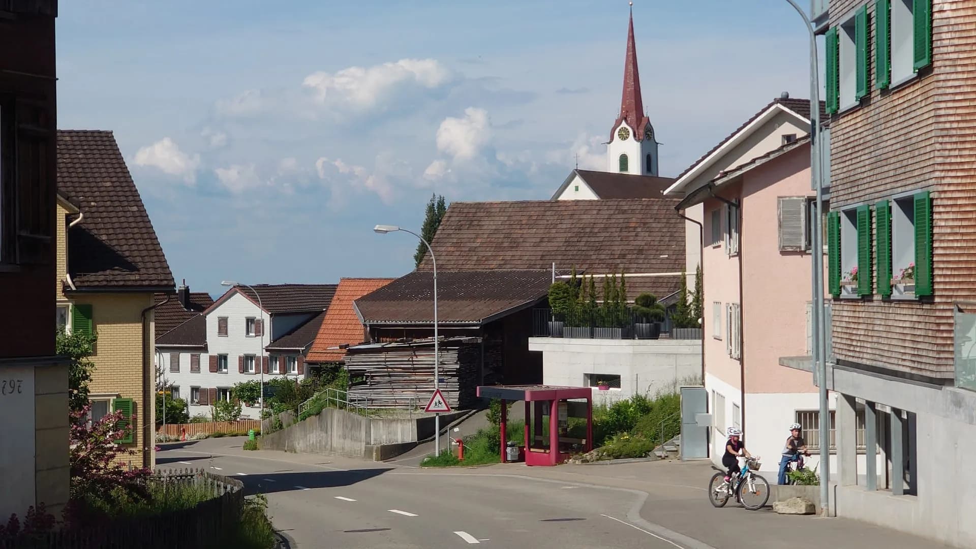 Cyclists riding past houses with green shutters in the village of Untereggen.