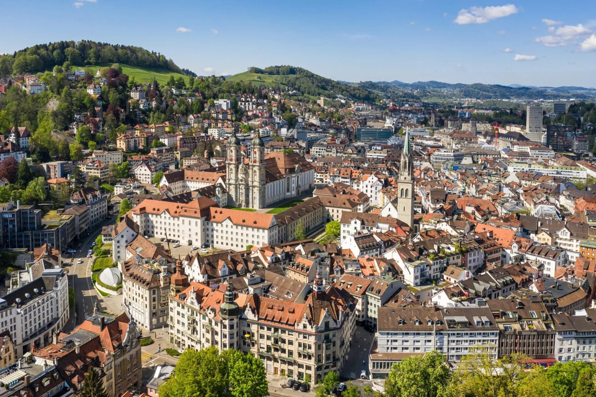 Aerial view of the town of St. Gallen with historic buildings and green hills under a blue sky.