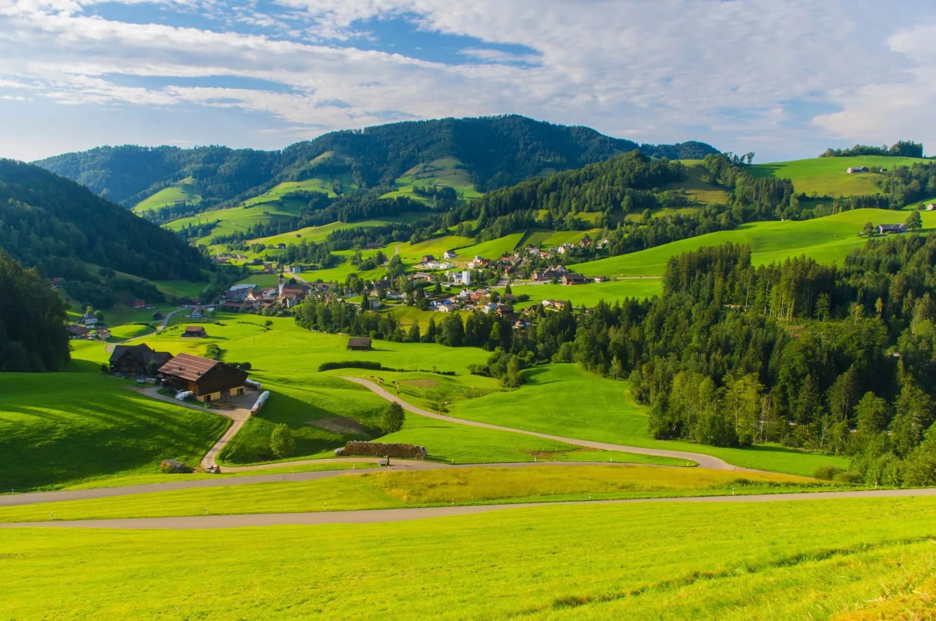 Village of St. Peterzell nestled in lush green rolling hills under a partly cloudy sky.