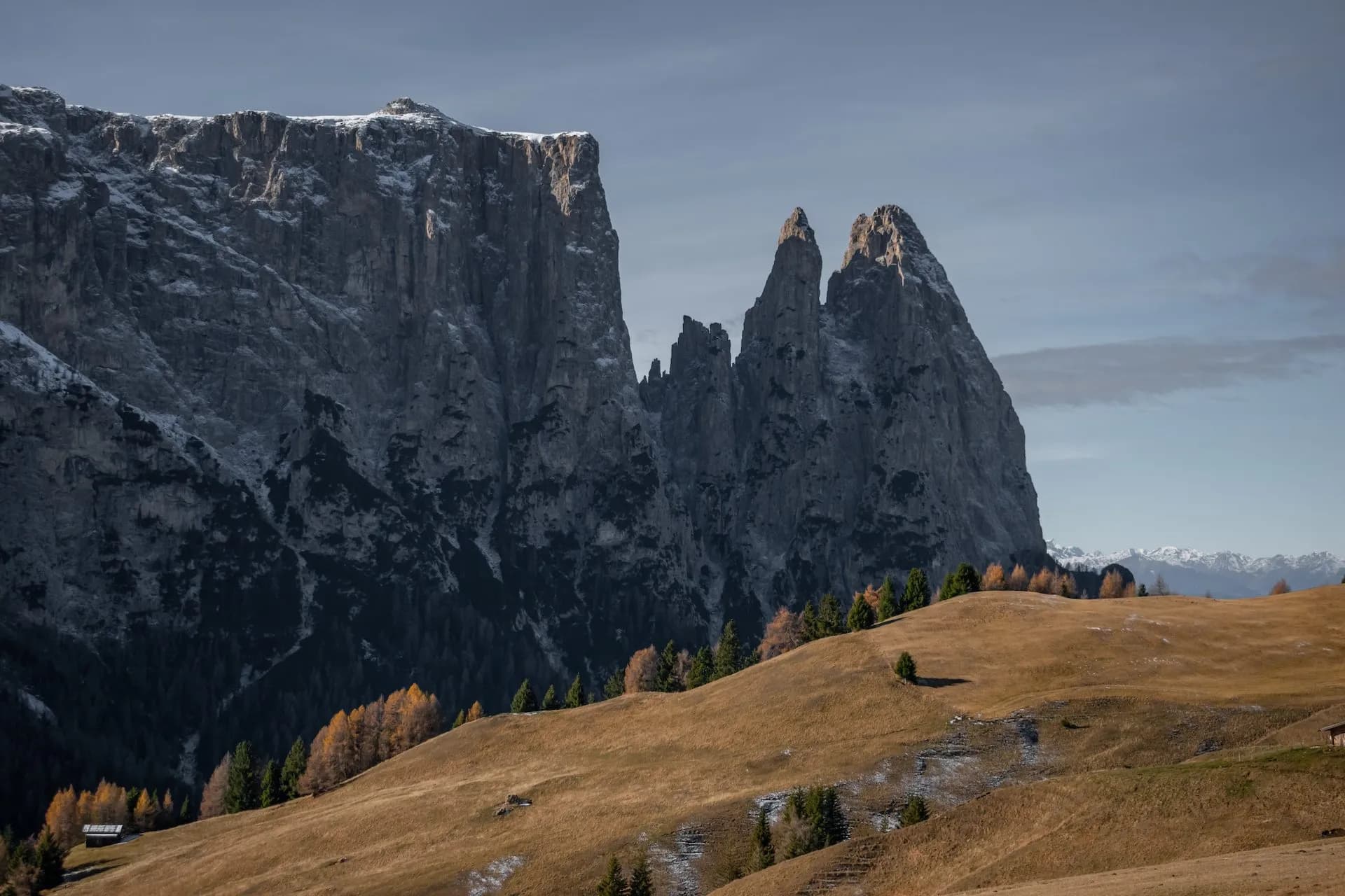 Dramatic rocky mountain peaks above rolling autumn hillside with sparse snow near Compatsch.
