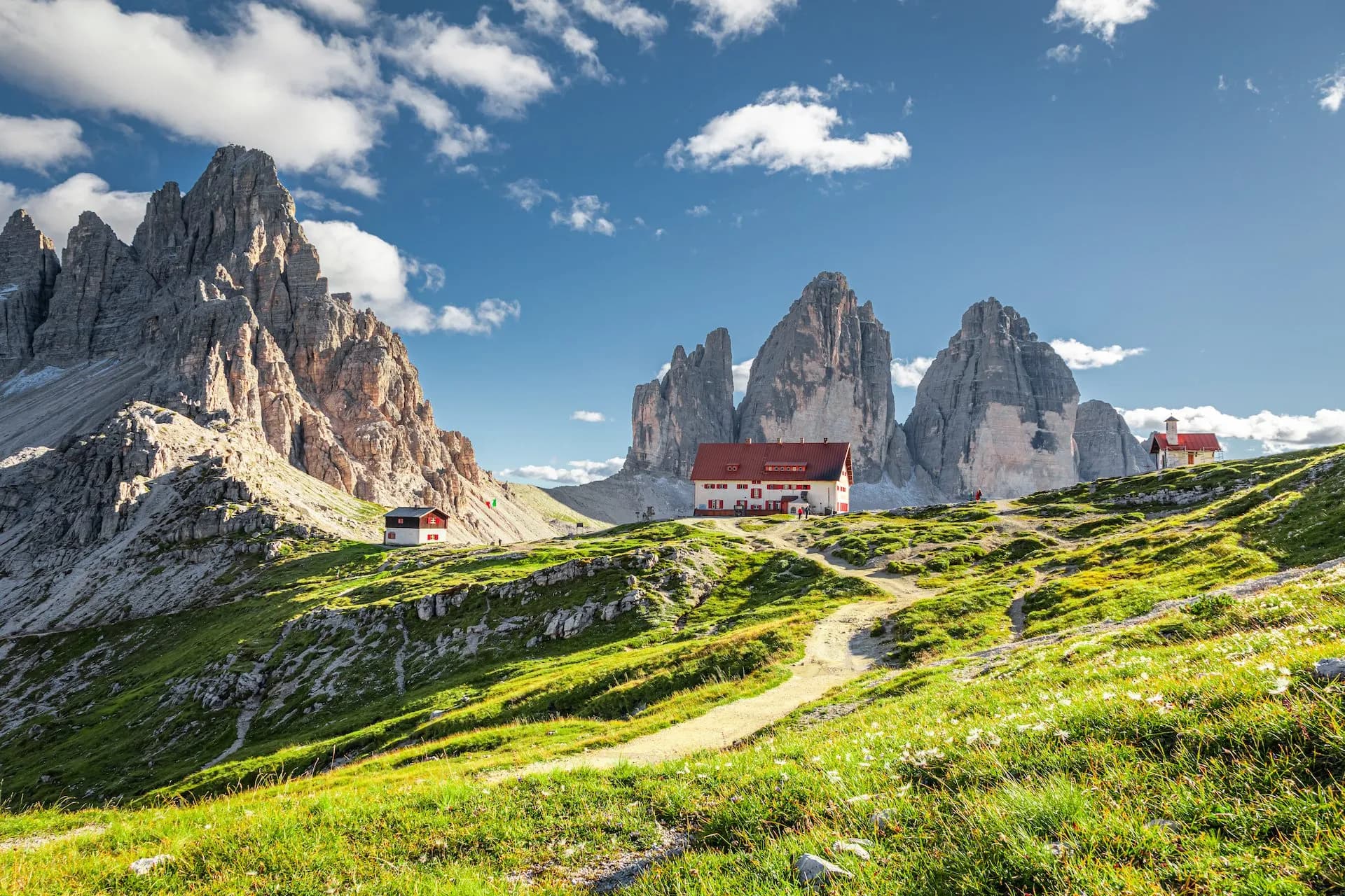 Tre Cime di Lavaredo peaks with mountain huts on grassy slope under blue sky