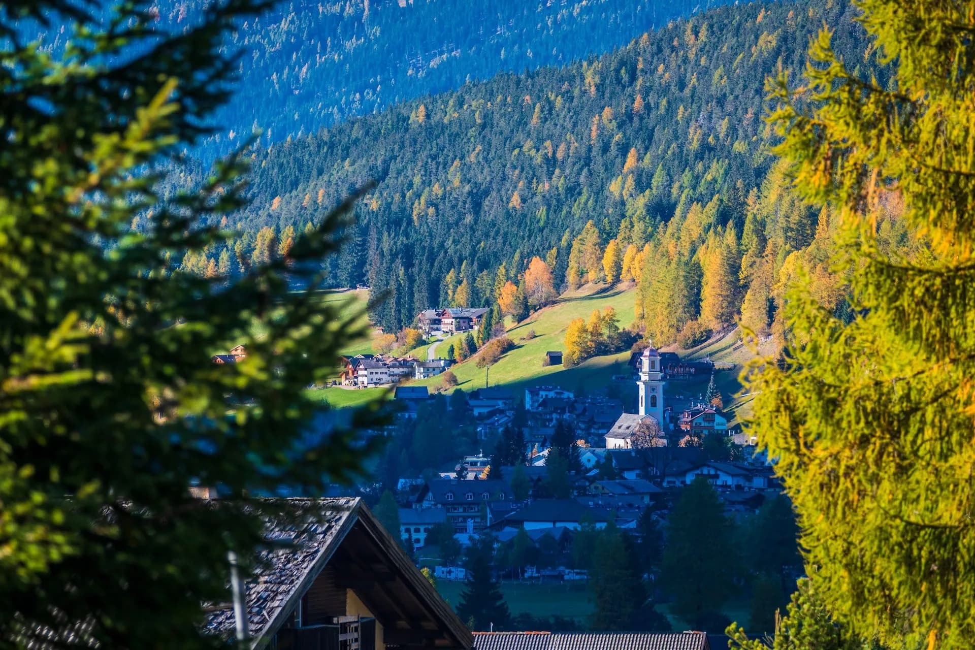 Alpine village nestled in valley with autumn foliage, viewed through foreground trees