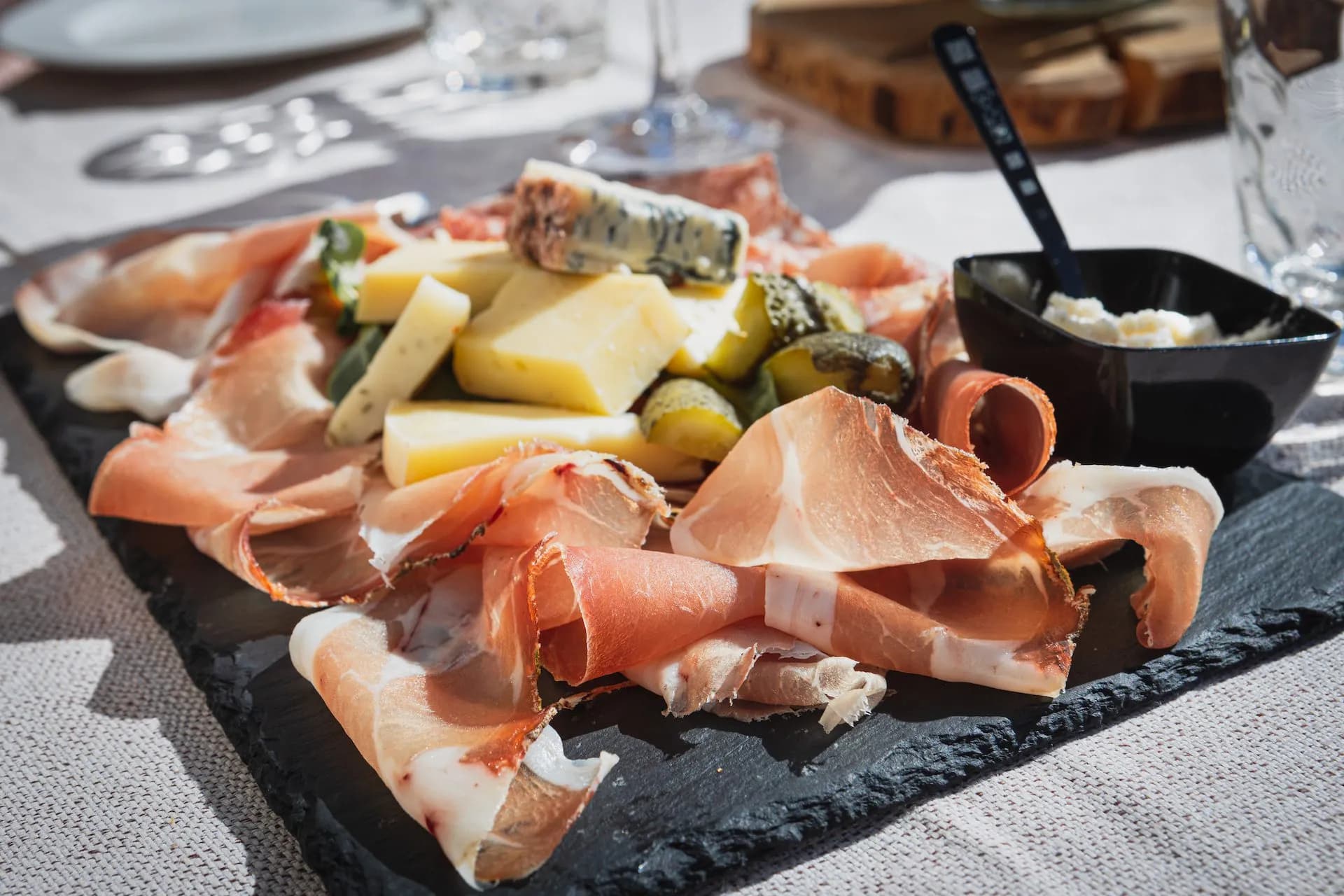 Charcuterie board with prosciutto, cheese, pickles, and spread on slate outdoors in the Dolomites.