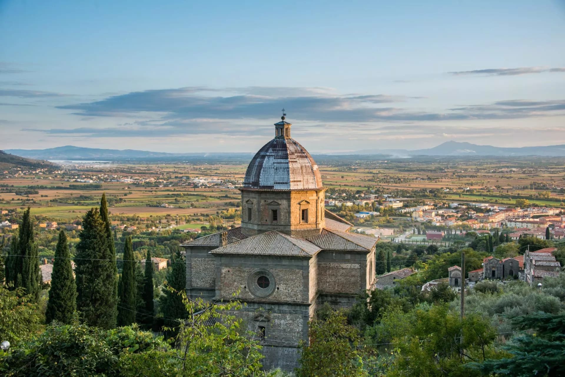 Stone church with a dome overlooking the Tuscan valley and distant mountains near Cortona.