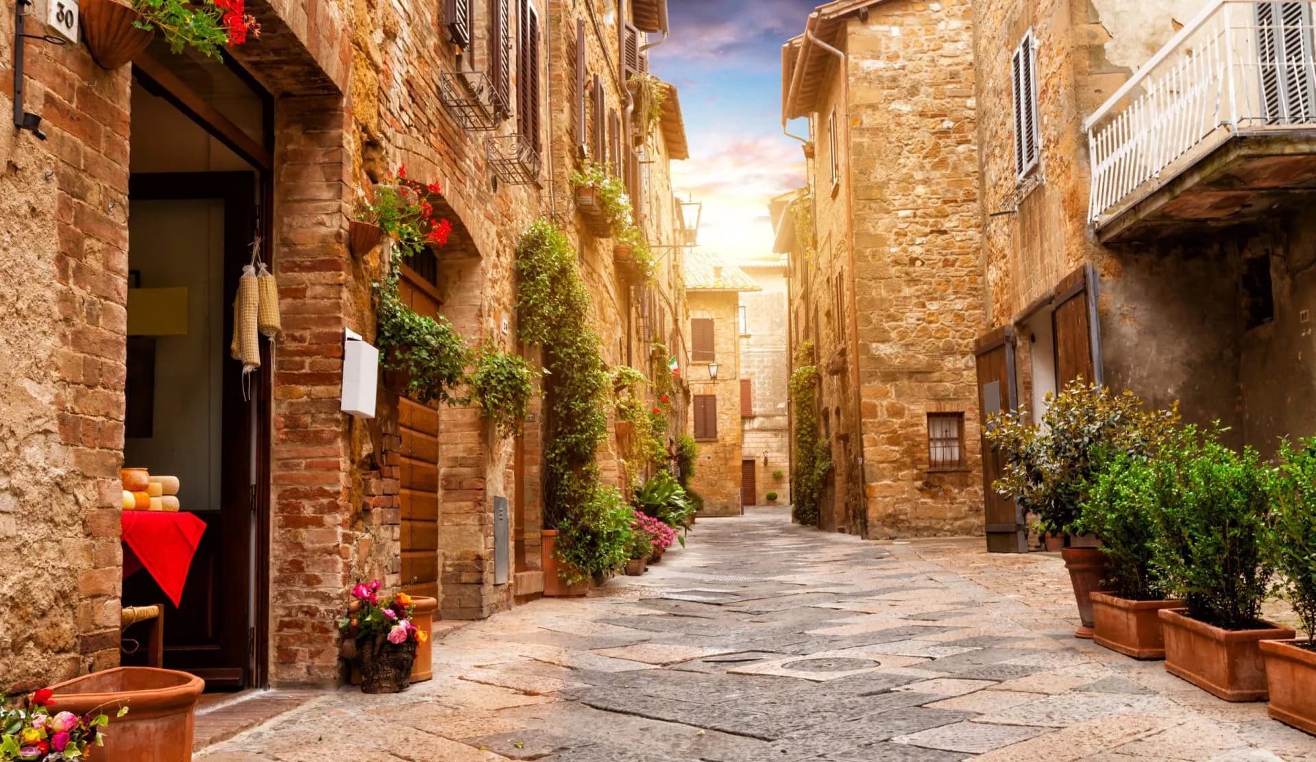 Cobblestone alley in a historic Italian town with stone buildings and potted plants, Tuscany.