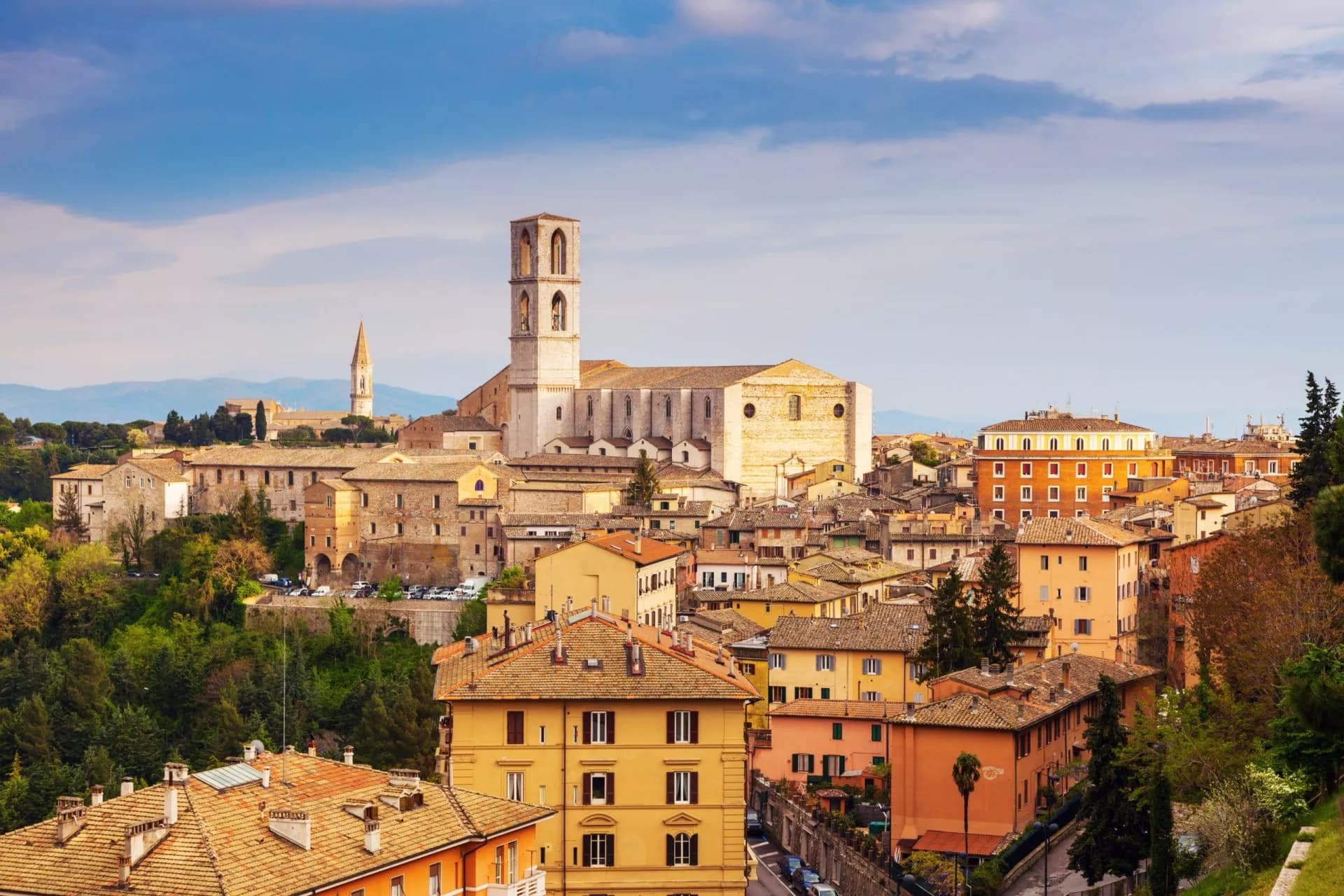 Perugia cityscape with historic buildings, large church tower, and rolling hills under a blue sky.