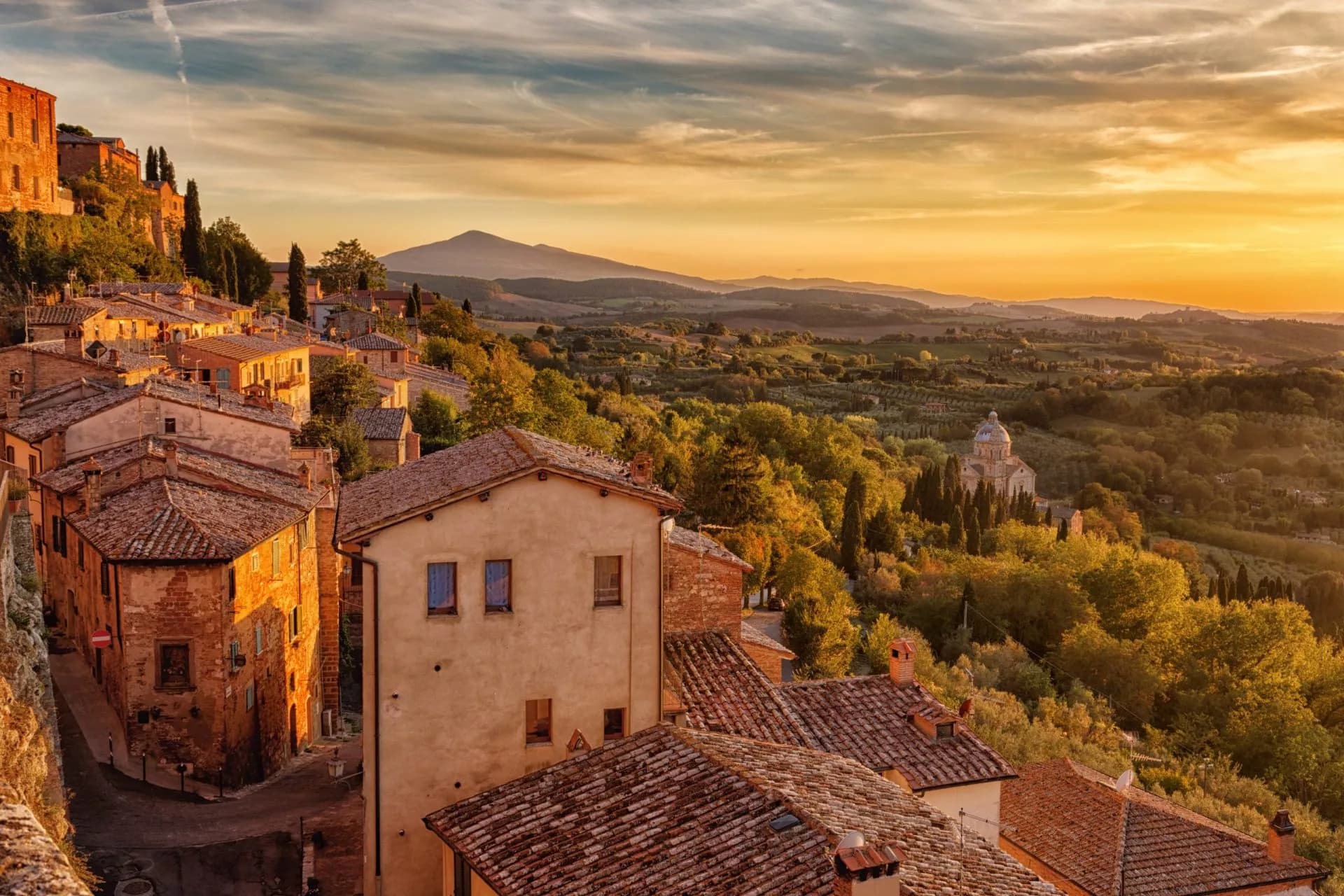 Historic Italian hillside town with terracotta roofs overlooking rolling hills at sunset