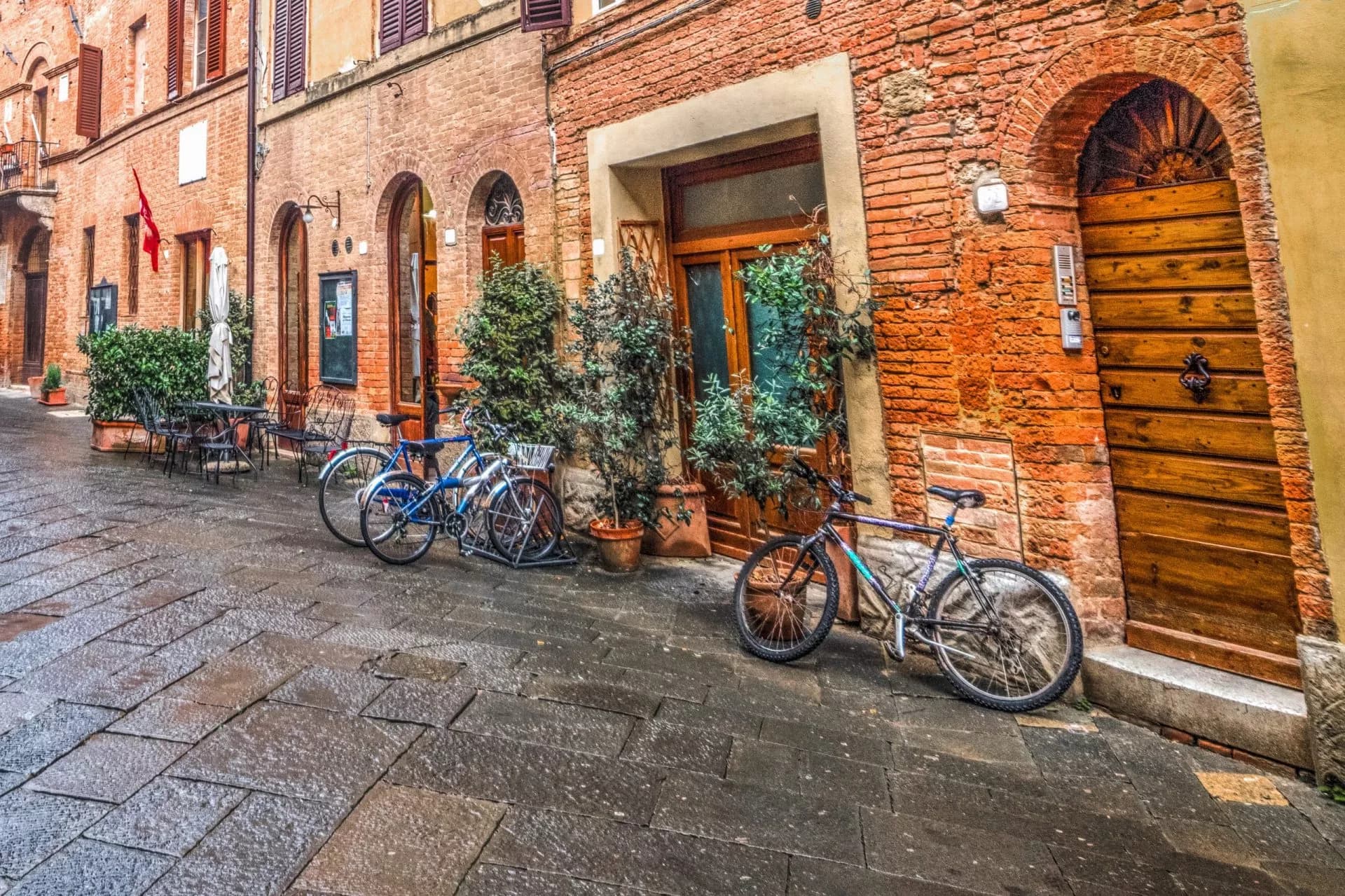 Bicycles parked on wet cobblestone street outside brick buildings in Buonconvento.