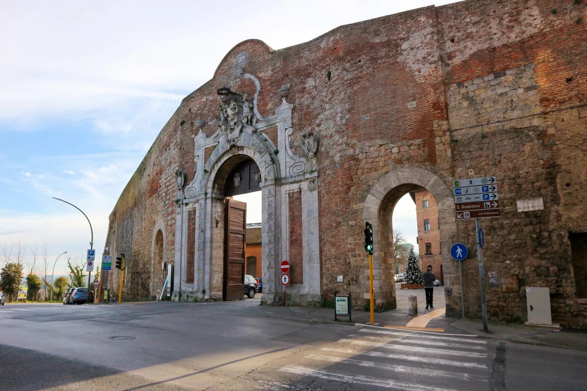 Porta Camollia, a large historic brick and stone city gate in Siena, with street signs and traffic light.