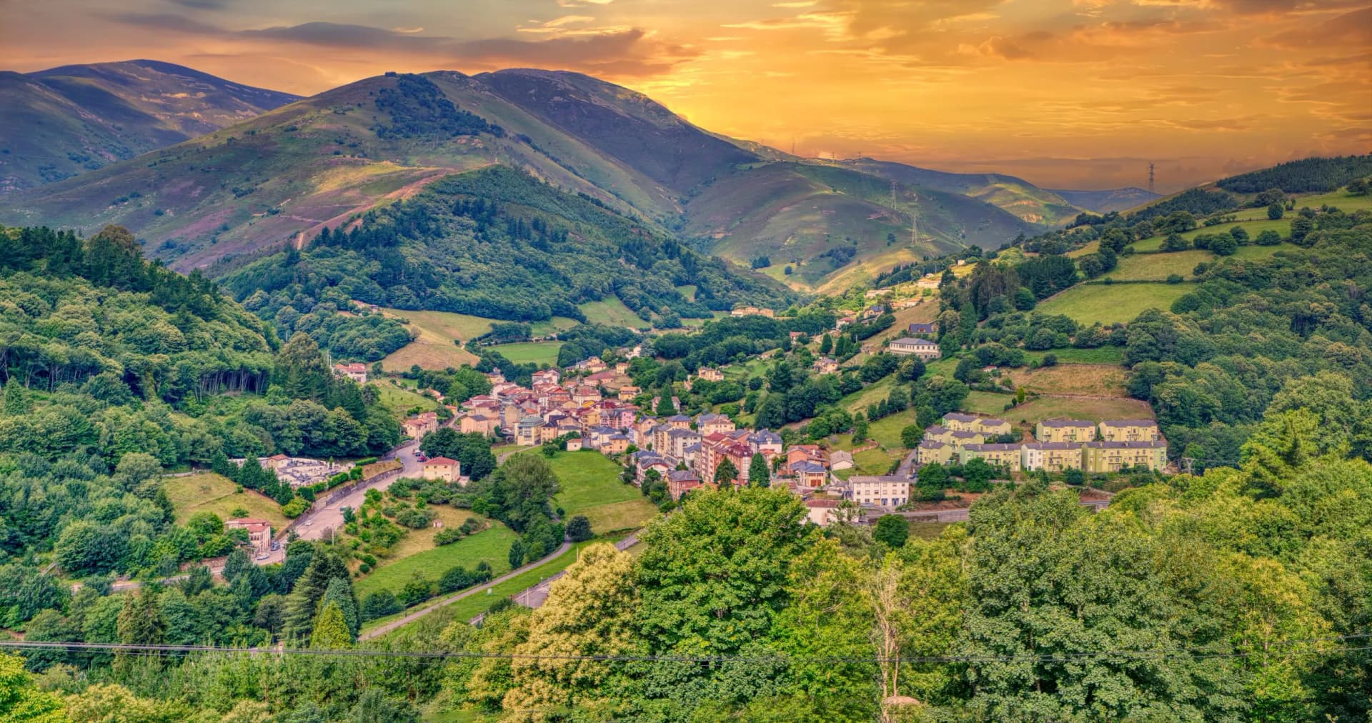 Panoramic view of Pola de Allande village nestled in lush green mountains at sunset.