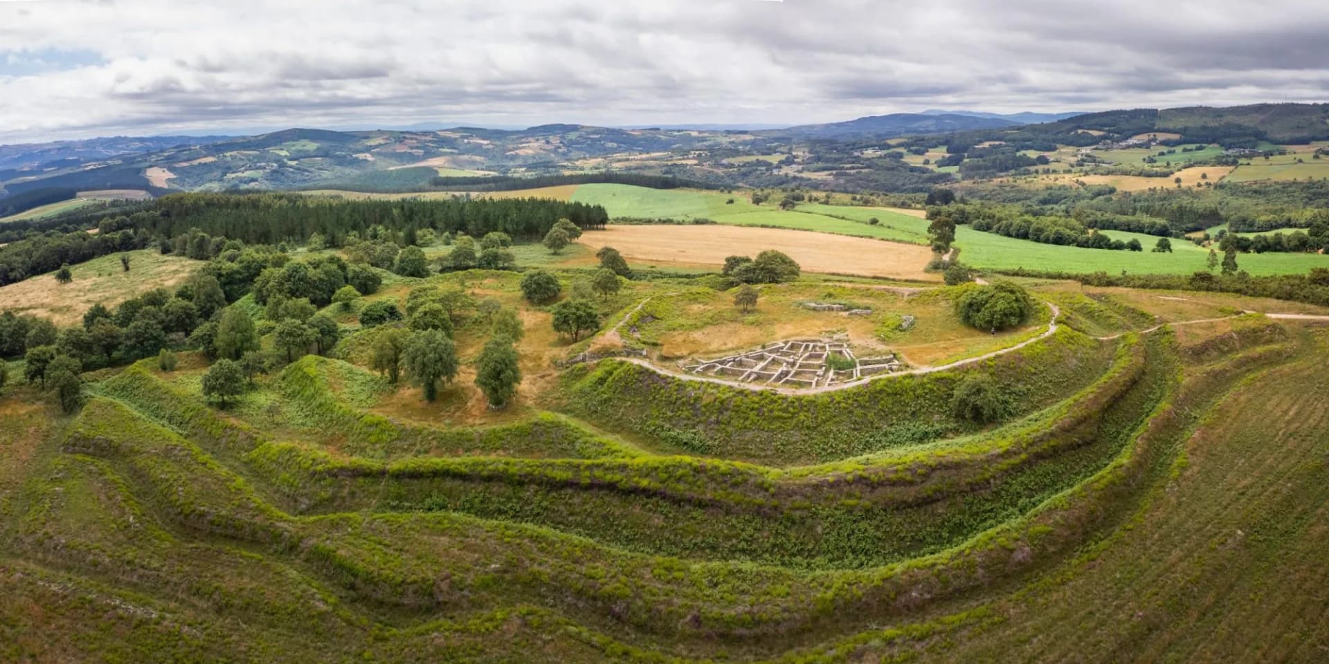 Hillfort ruins at Castro de Castromaior with concentric defensive earthworks and rolling green landscape.