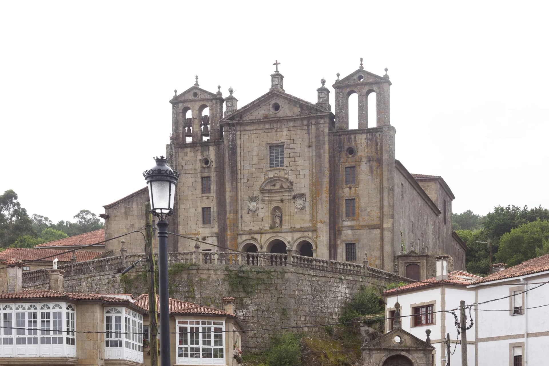 Stone church on a hill above white buildings with enclosed balconies in Padrón.