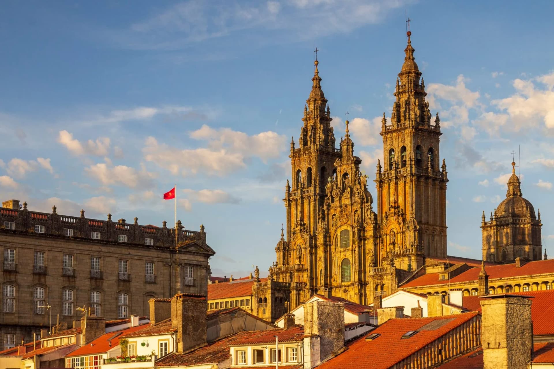 Santiago de Compostela Cathedral towers illuminated above terracotta rooftops under a blue sky.