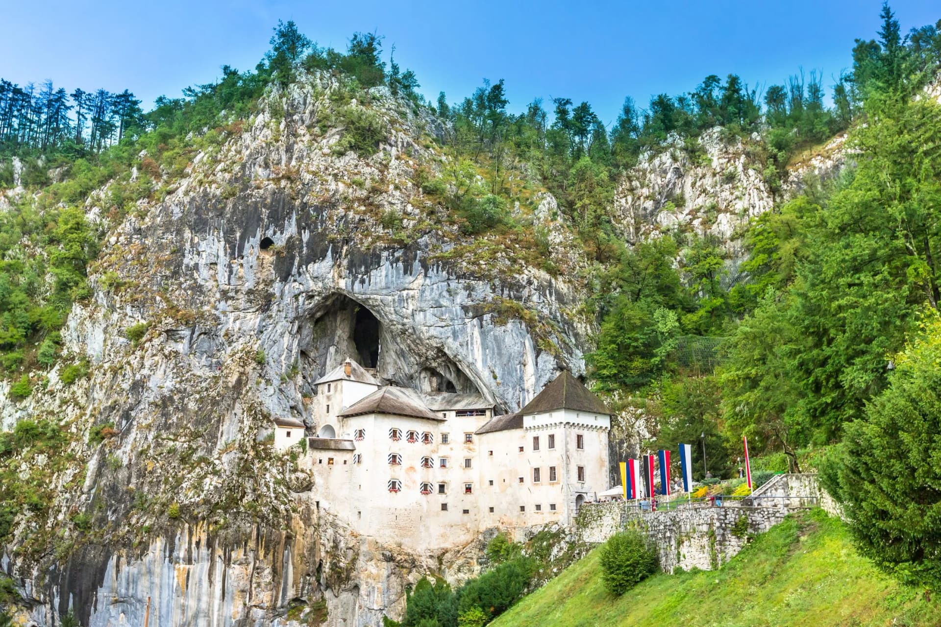 Predjama Castle built into a cliff face with a large cave entrance and green forested hillsides.