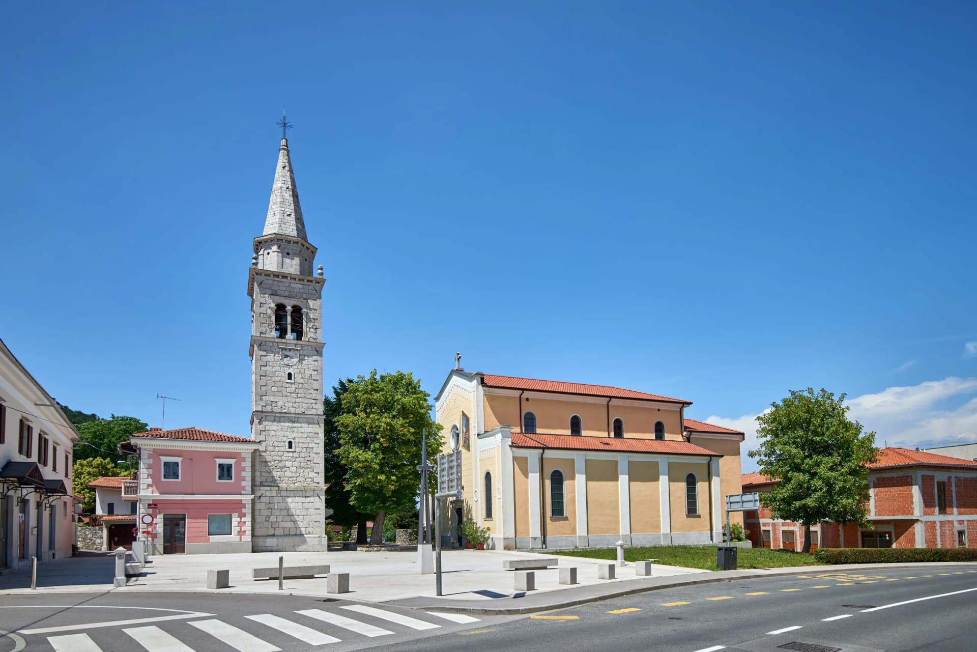Stone church tower and yellow church building in town square under clear blue sky