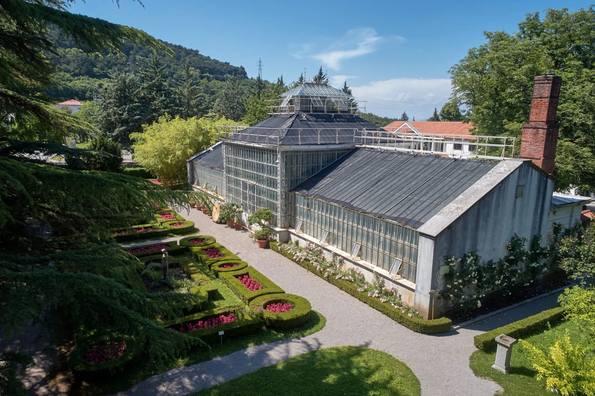 Greenhouse and formal gardens with manicured hedges and pink flowers at the Botanical Garden of Sežana.