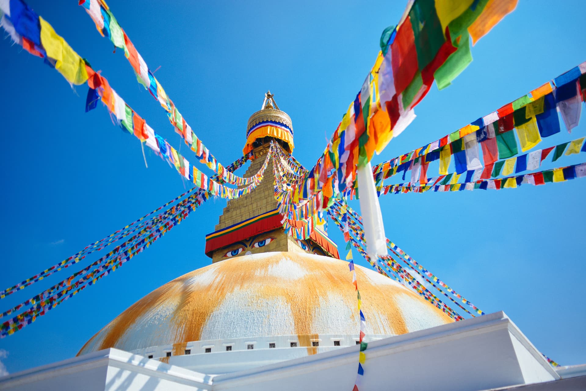 Boudhanath Stupa dome with painted eyes and colorful prayer flags against bright blue sky in Kathmandu.