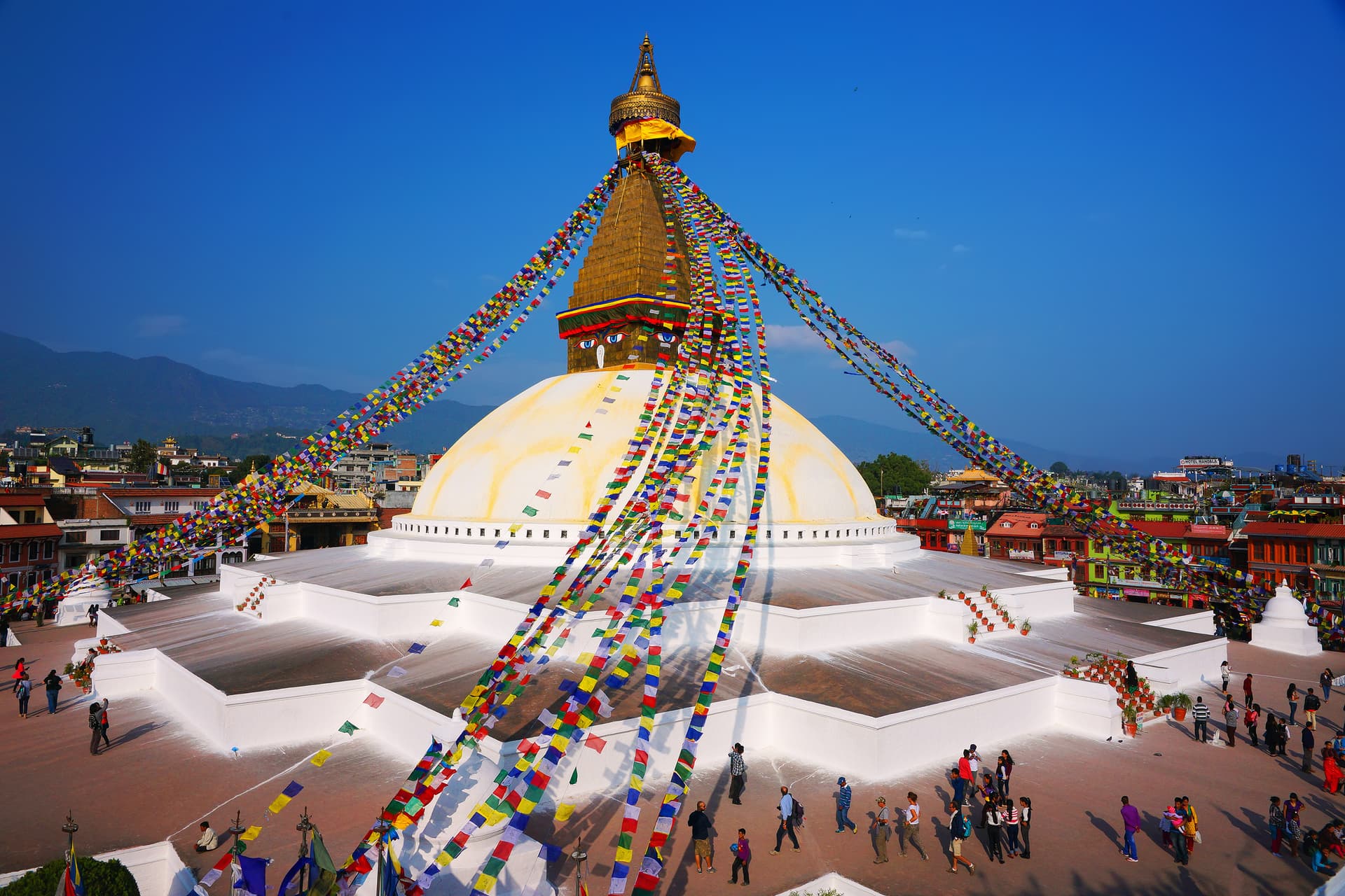 Boudhanath Stupa with golden spire and colorful prayer flags under a clear blue sky.