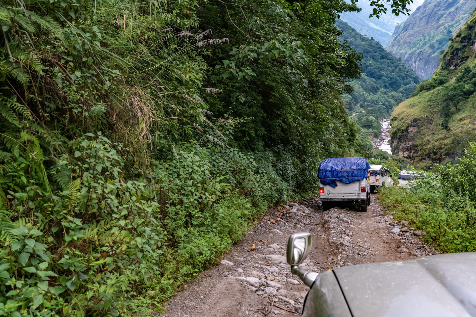 Vehicles driving on rocky dirt road through lush green mountain valley in Nepal