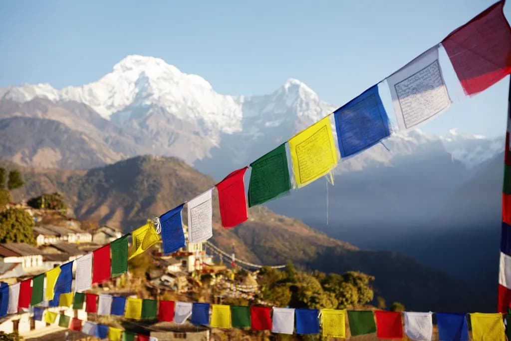 Colorful prayer flags strung across a view of snow-capped Himalayan mountains and a village.