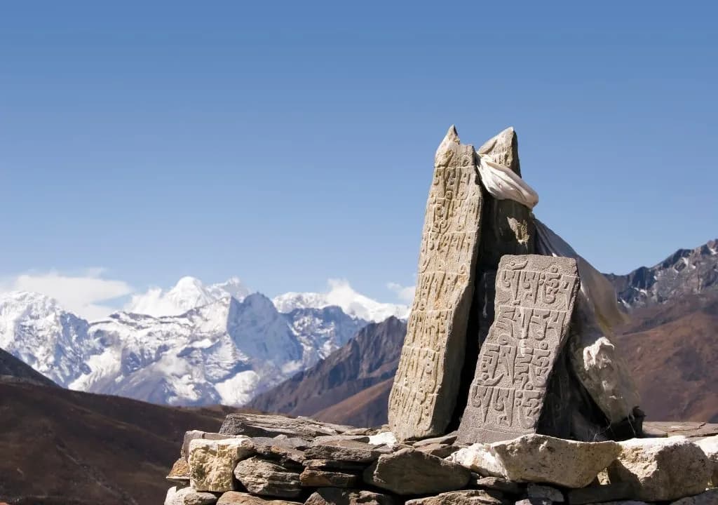 Buddhist mani stones with prayer flags against a backdrop of snow-capped Himalayan mountains.