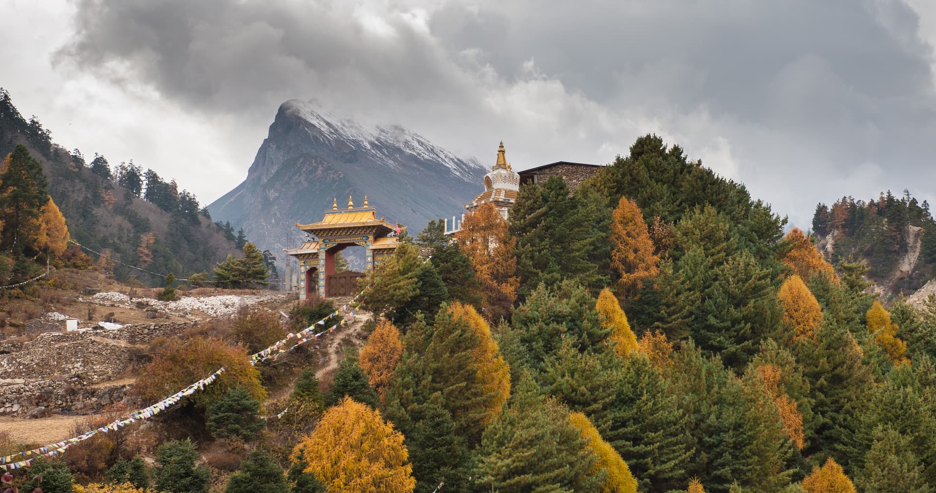 Gompa gate and stupa above Lho village with autumn trees and snow-capped mountain.