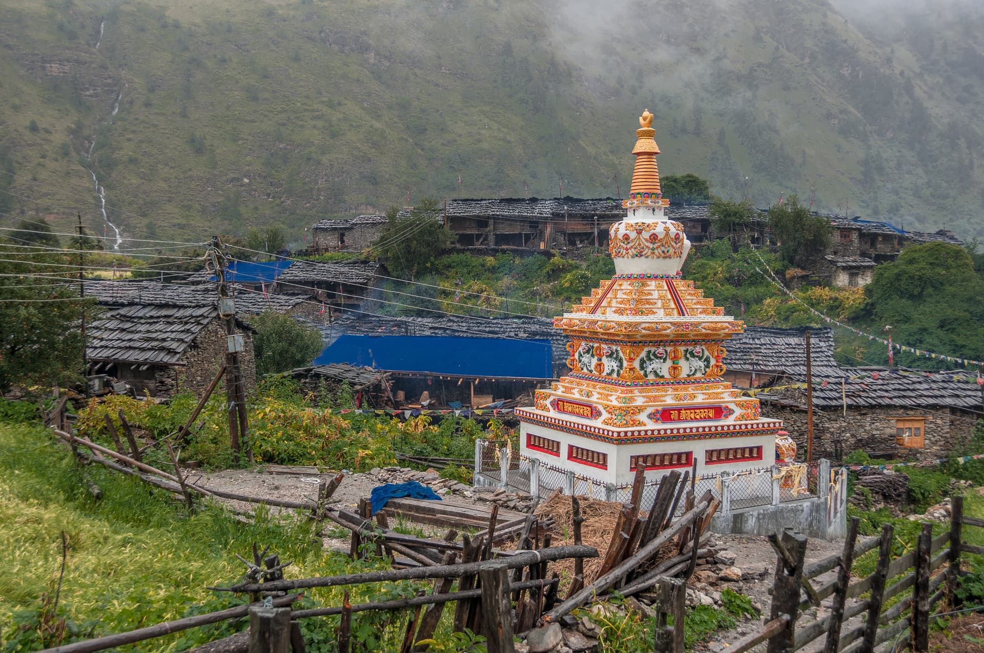 Ornate Buddhist stupa in Lho Gaon village with stone houses and green mountain backdrop.