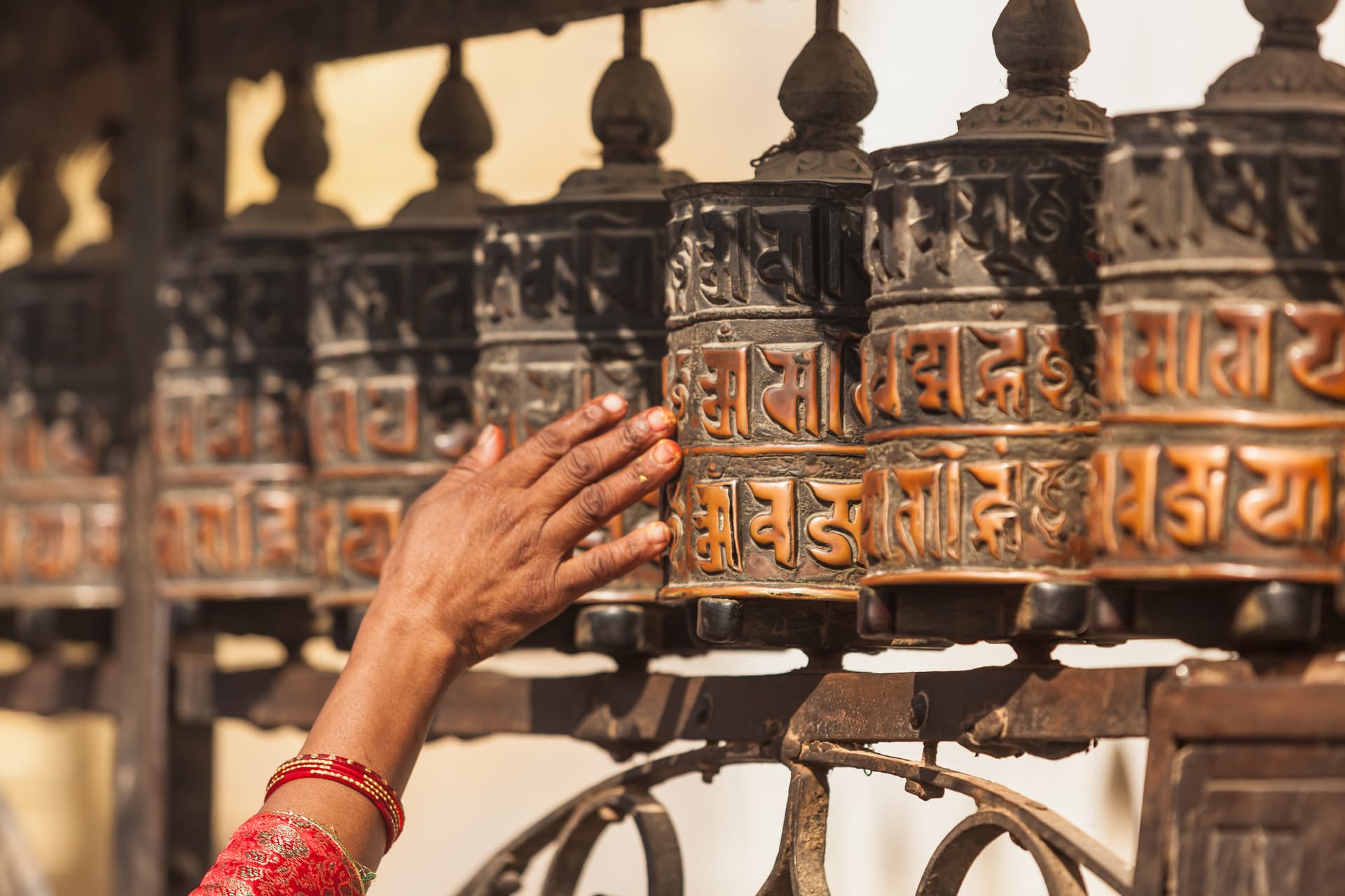 Hand turning row of engraved Tibetan prayer wheels with Sanskrit script.