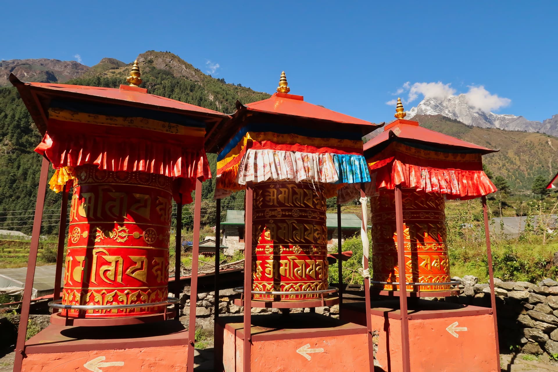 Three large red prayer wheels in Lukla with mountains and clear blue sky.