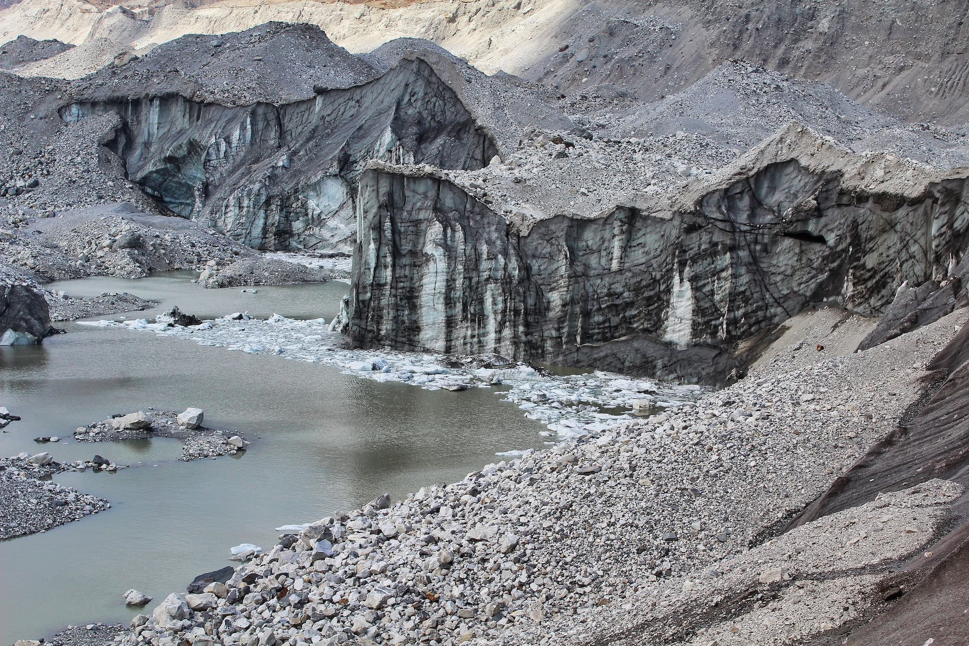 Melt pools with ice chunks next to the dark, rocky face of the Ngozumpa Glacier.