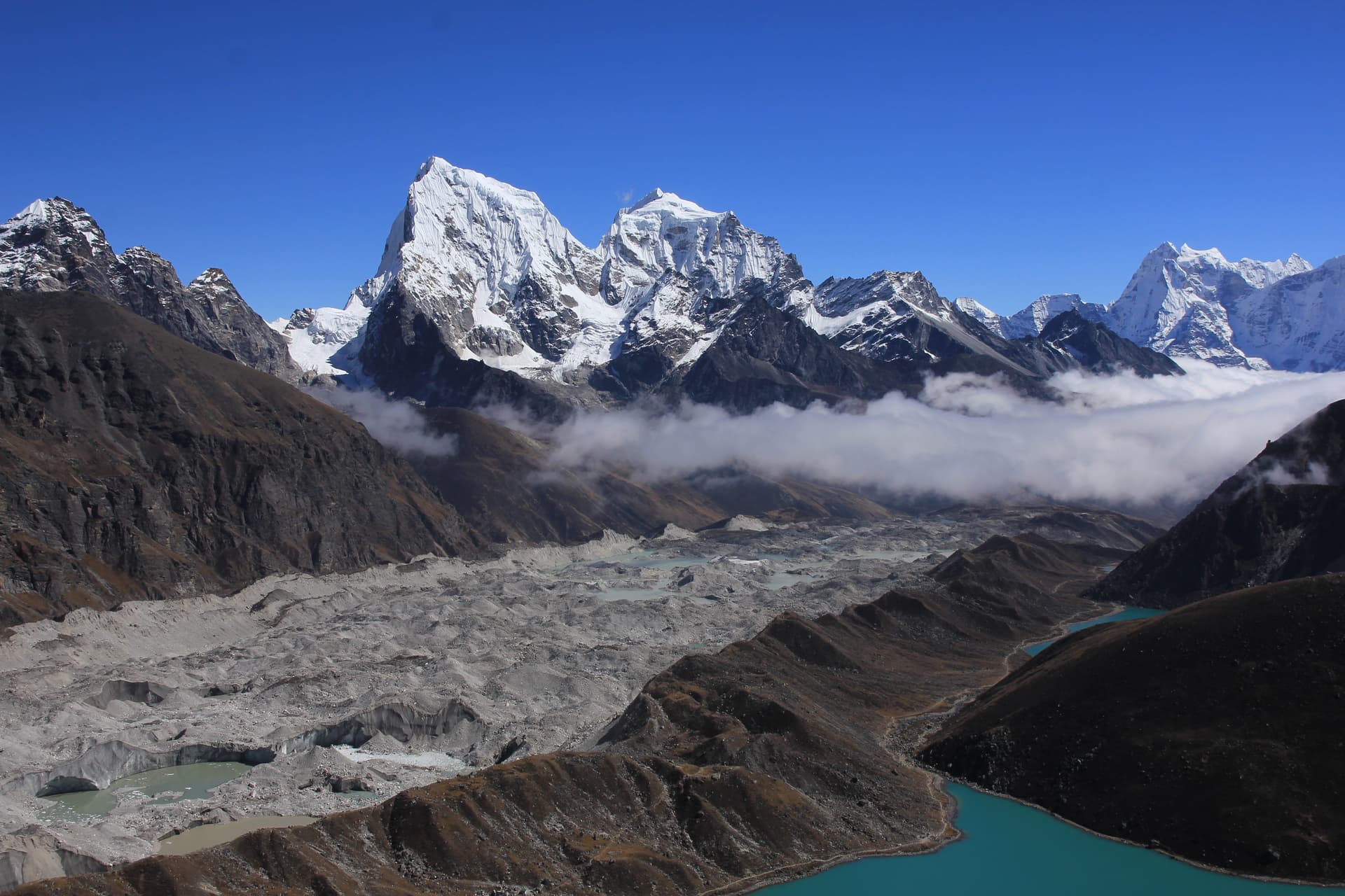 Glacier and turquoise lakes below snow-capped Mount Cholatse under clear blue sky.