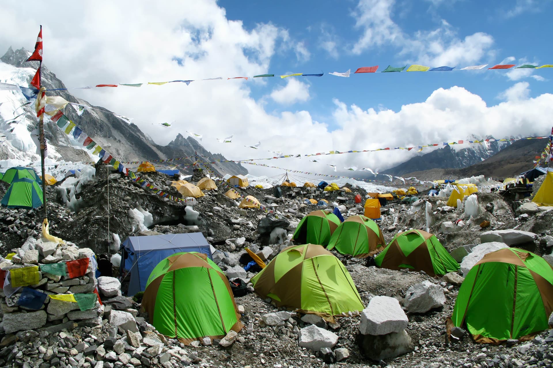 Tents at Everest Base Camp with prayer flags, ice, and rocky terrain under a cloudy sky.