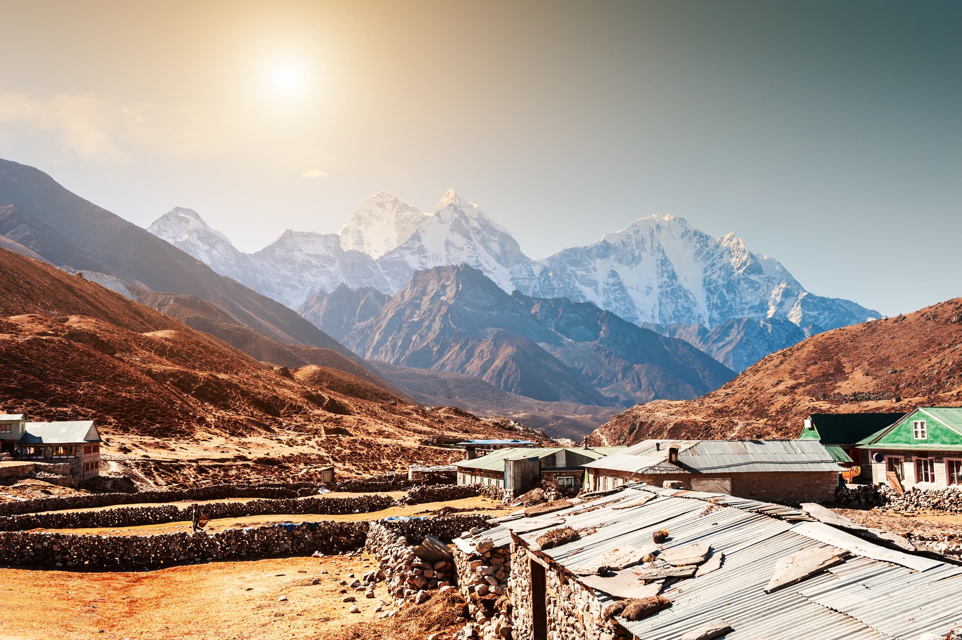 Pheriche village with stone walls and corrugated roofs set against massive snow-capped Himalayan mountains.
