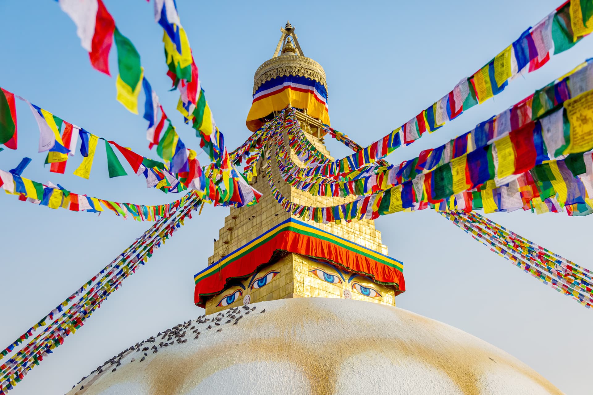 Stupa with Buddha eyes and colorful prayer flags against clear blue sky in Kathmandu