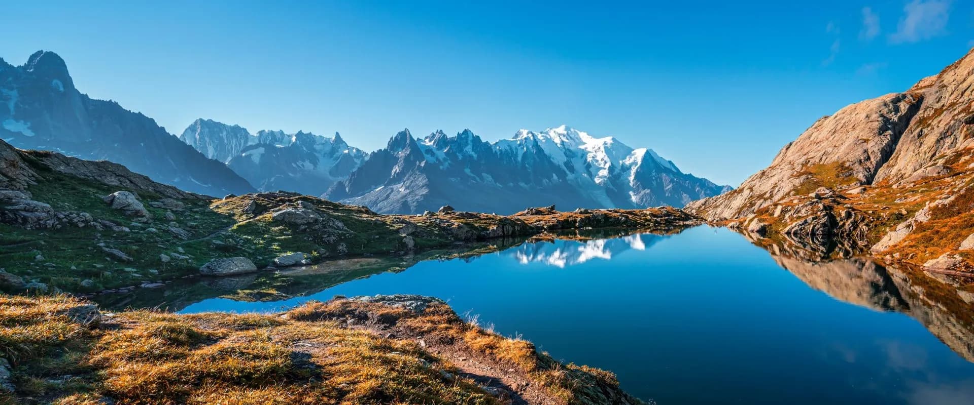 Alpine lake reflecting snow-capped Mont Blanc massif under a clear blue sky