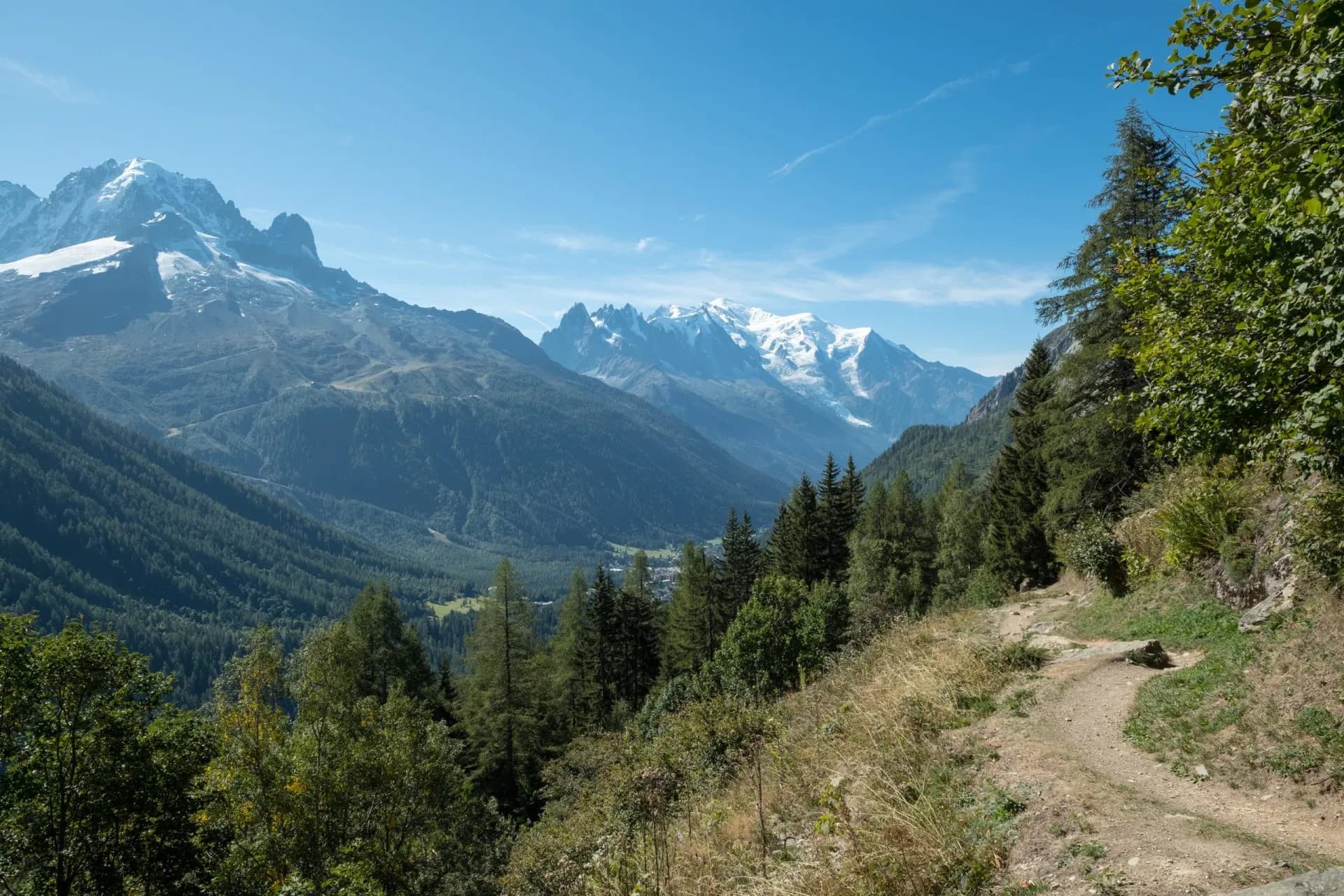 Hiking trail overlooking Aiguillette des Posettes with snow-capped Alps and forested valley.