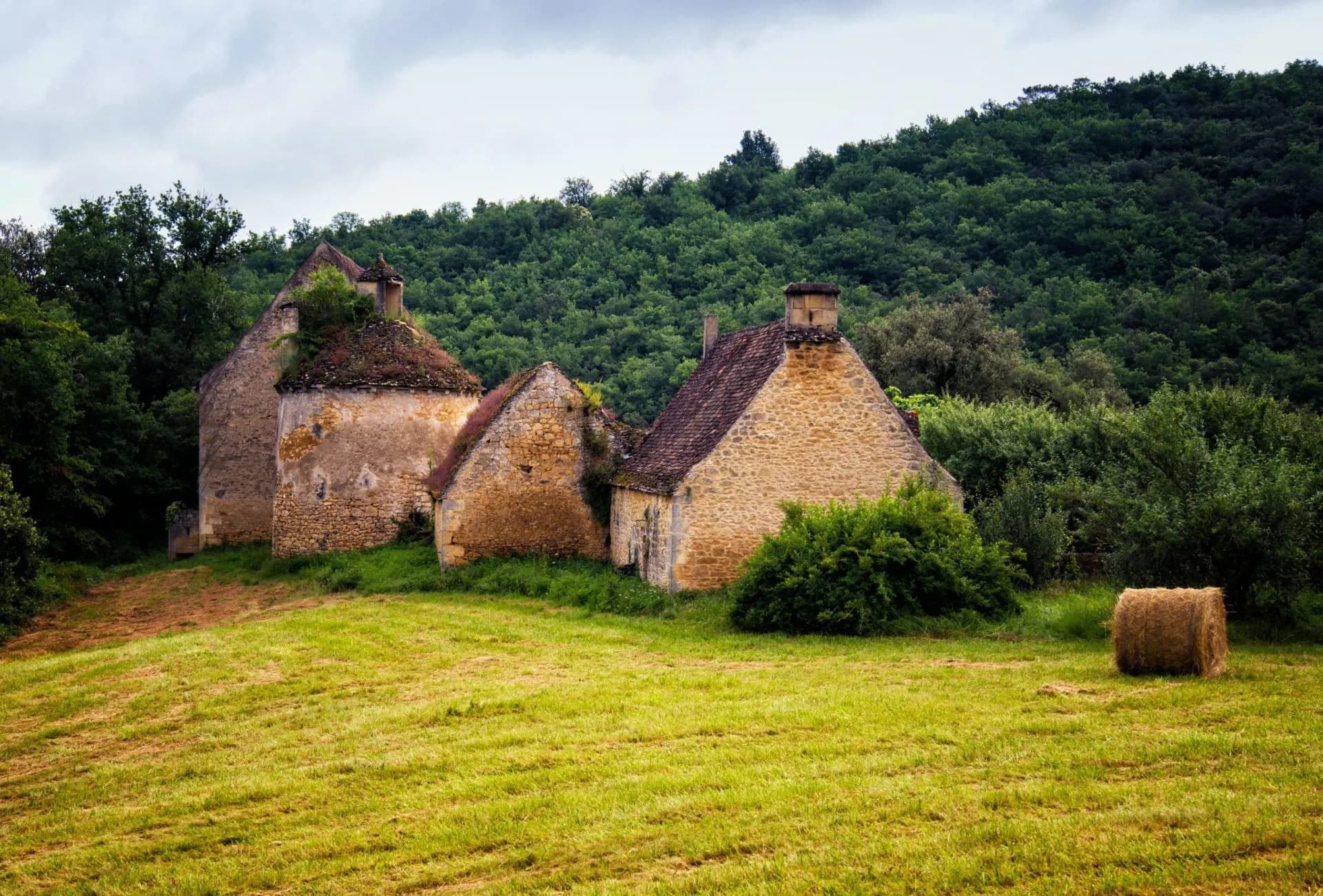 Abandoned stone farmhouse ruins in a field with a hay bale, Dordogne Valley.