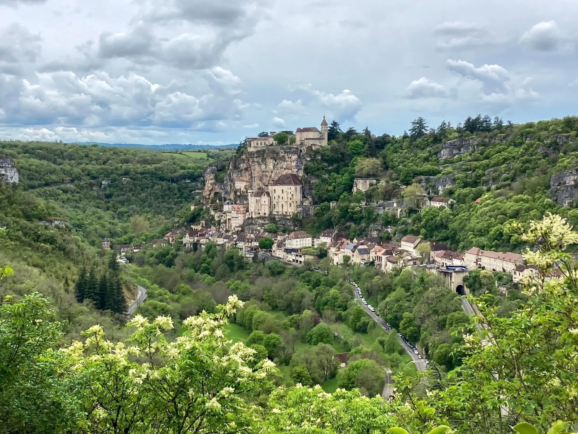 Rocamadour village built into a cliffside overlooking a lush green valley under cloudy skies.