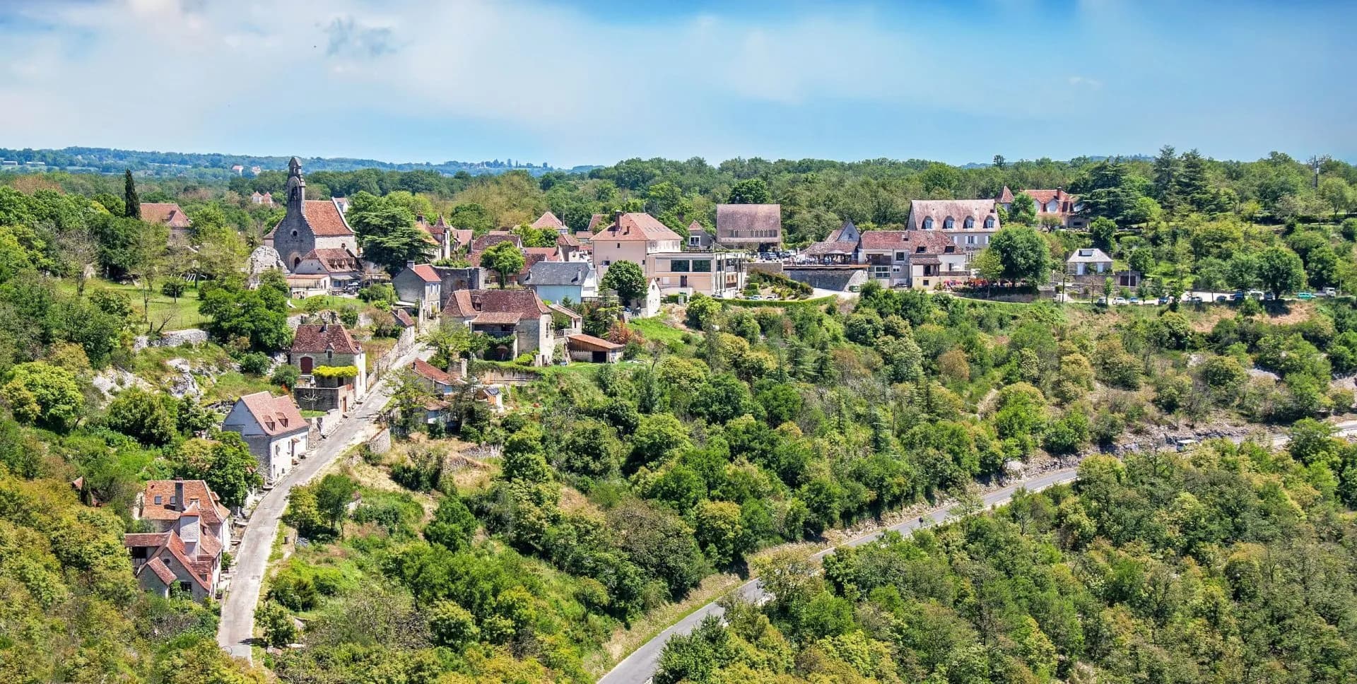 Village with stone church nestled in lush green hillside, L'Hospitalet in Dordogne.