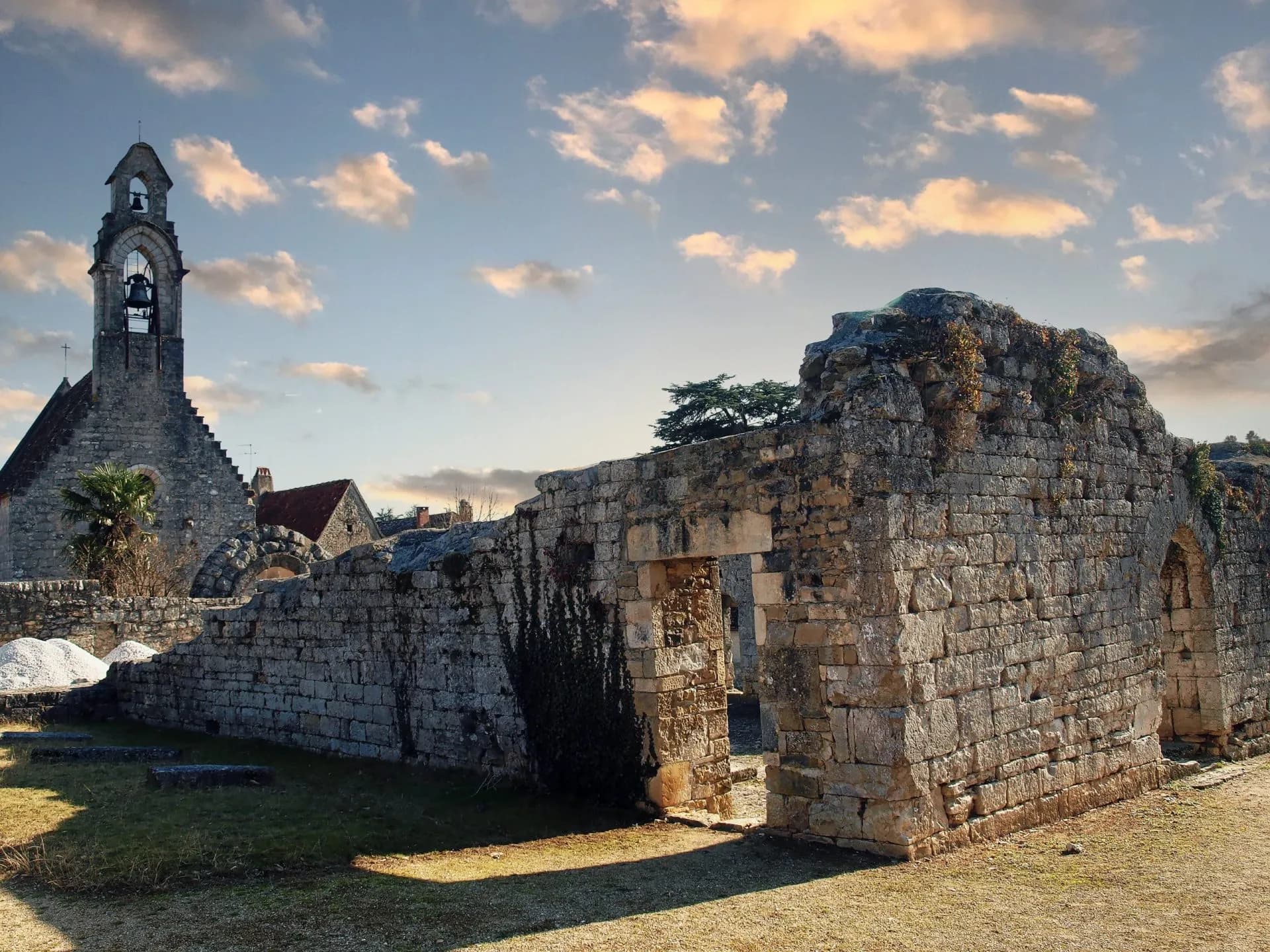 Stone ruins and church bell tower under a dramatic sky at Hameau de L'Hospitalet.