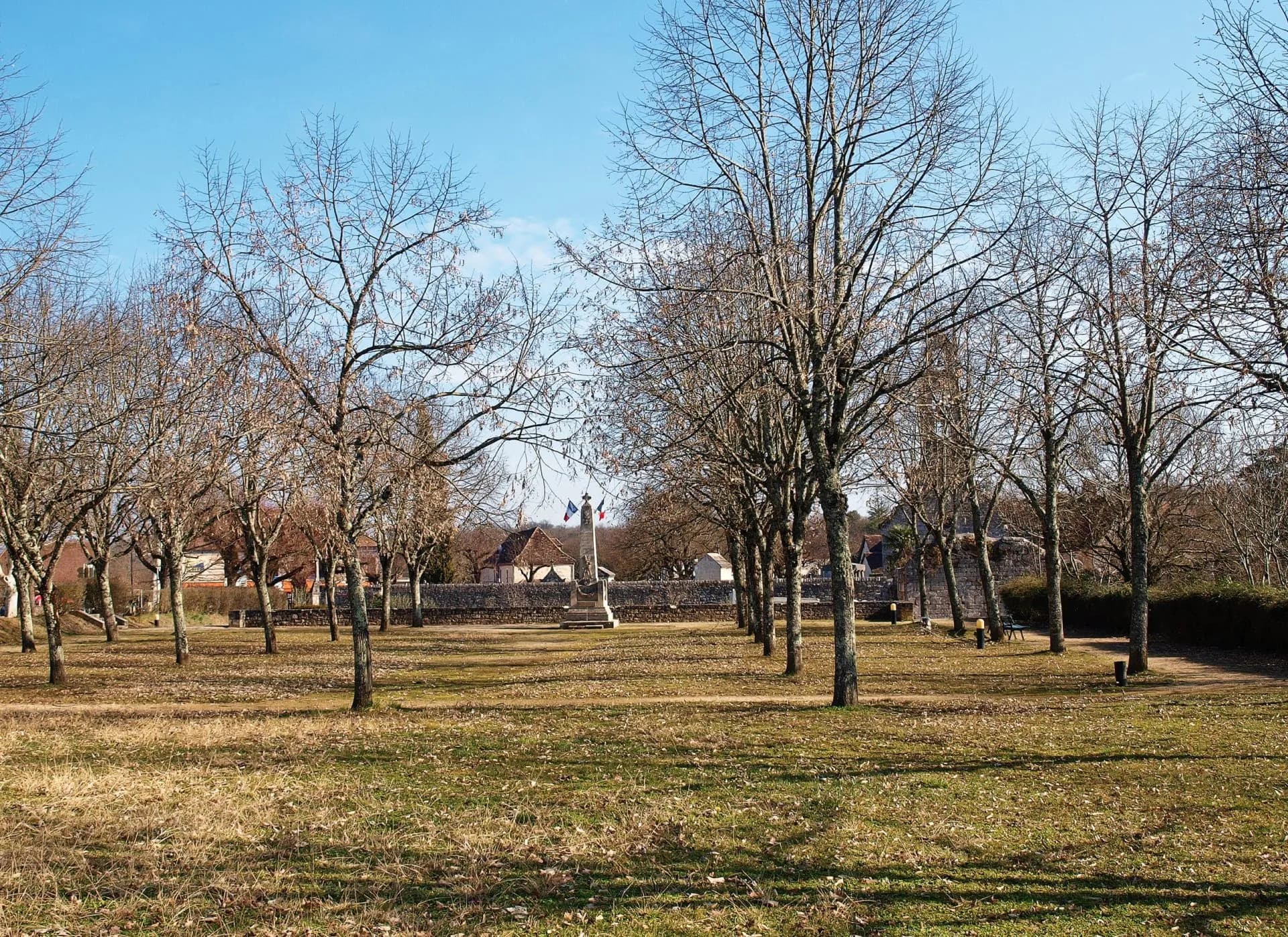 Park with bare trees in winter, war memorial with French flags, L'Hospitalet-du-Larzac.