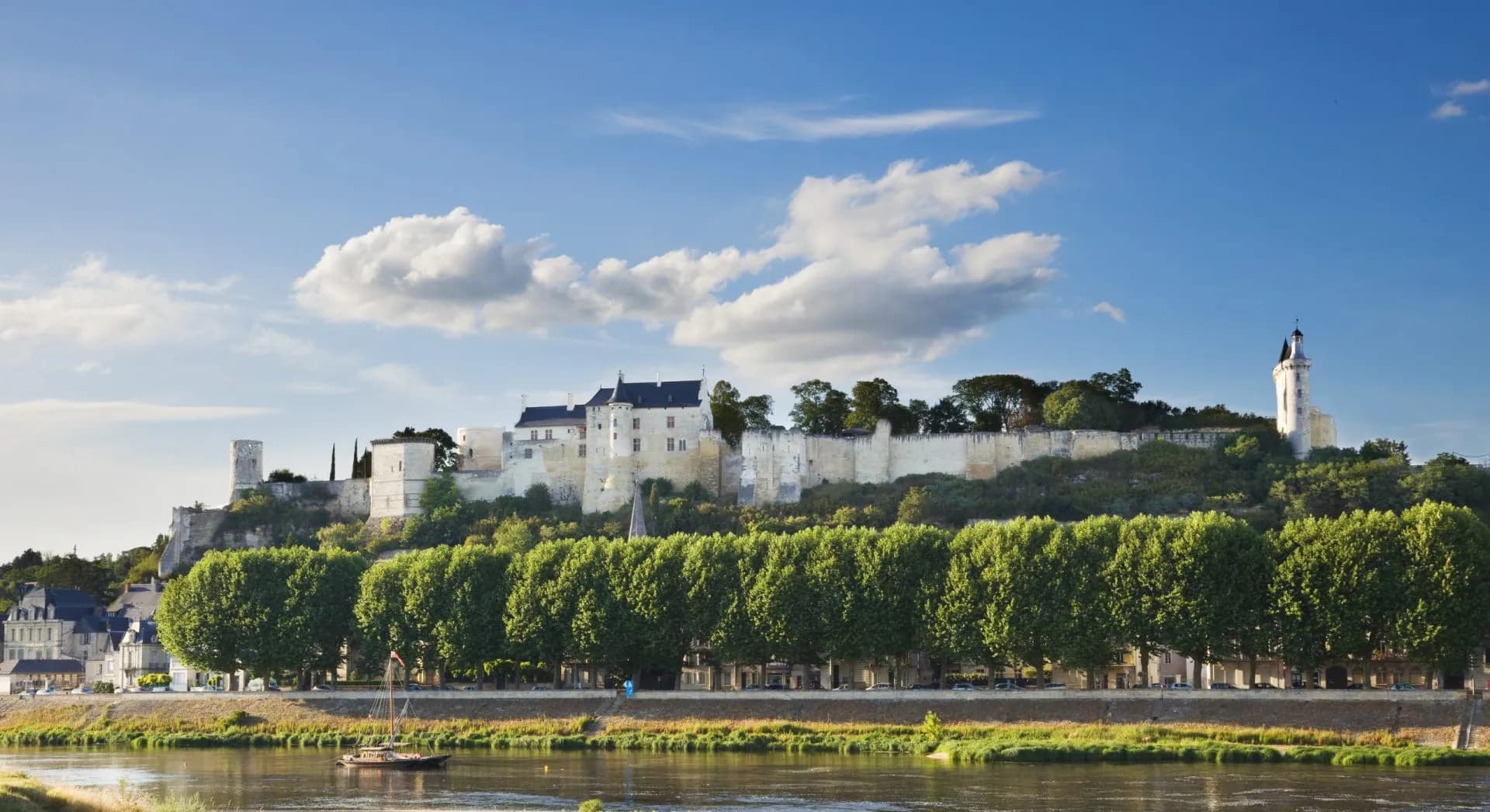 Chateau du Chinon overlooking the river with a small sailboat under a blue sky.