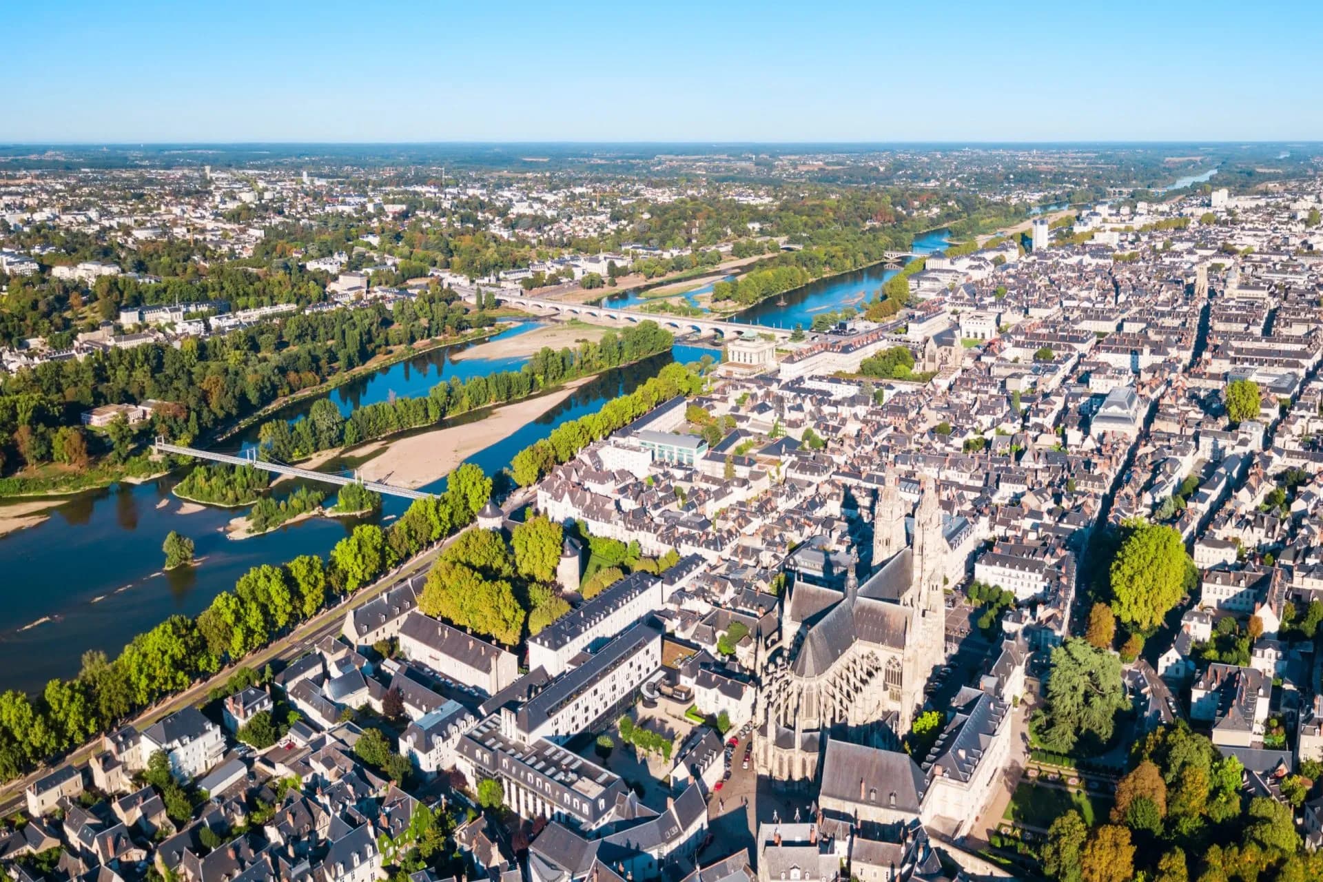 Aerial view of historic European city with cathedral, dense rooftops, and wide river with bridges.