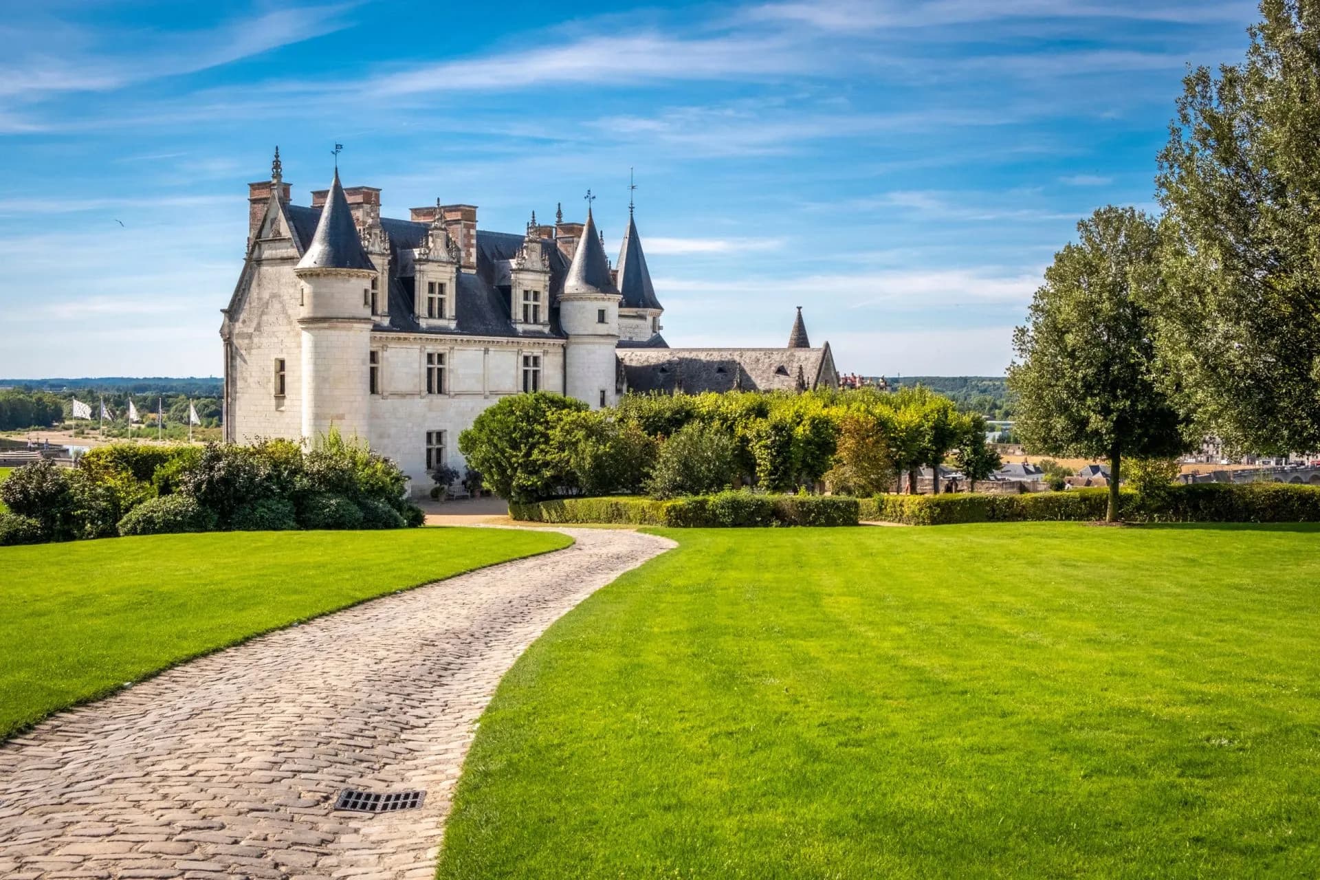 Chateau d'Amboise with cobblestone path and vibrant green lawn under blue sky.