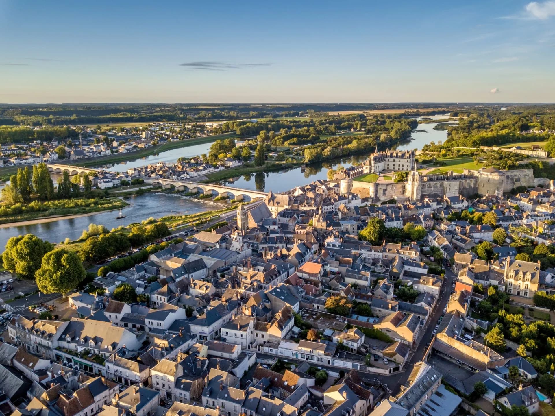 Aerial view of Amboise town with dense rooftops, the Loire River, and a historic chateau.