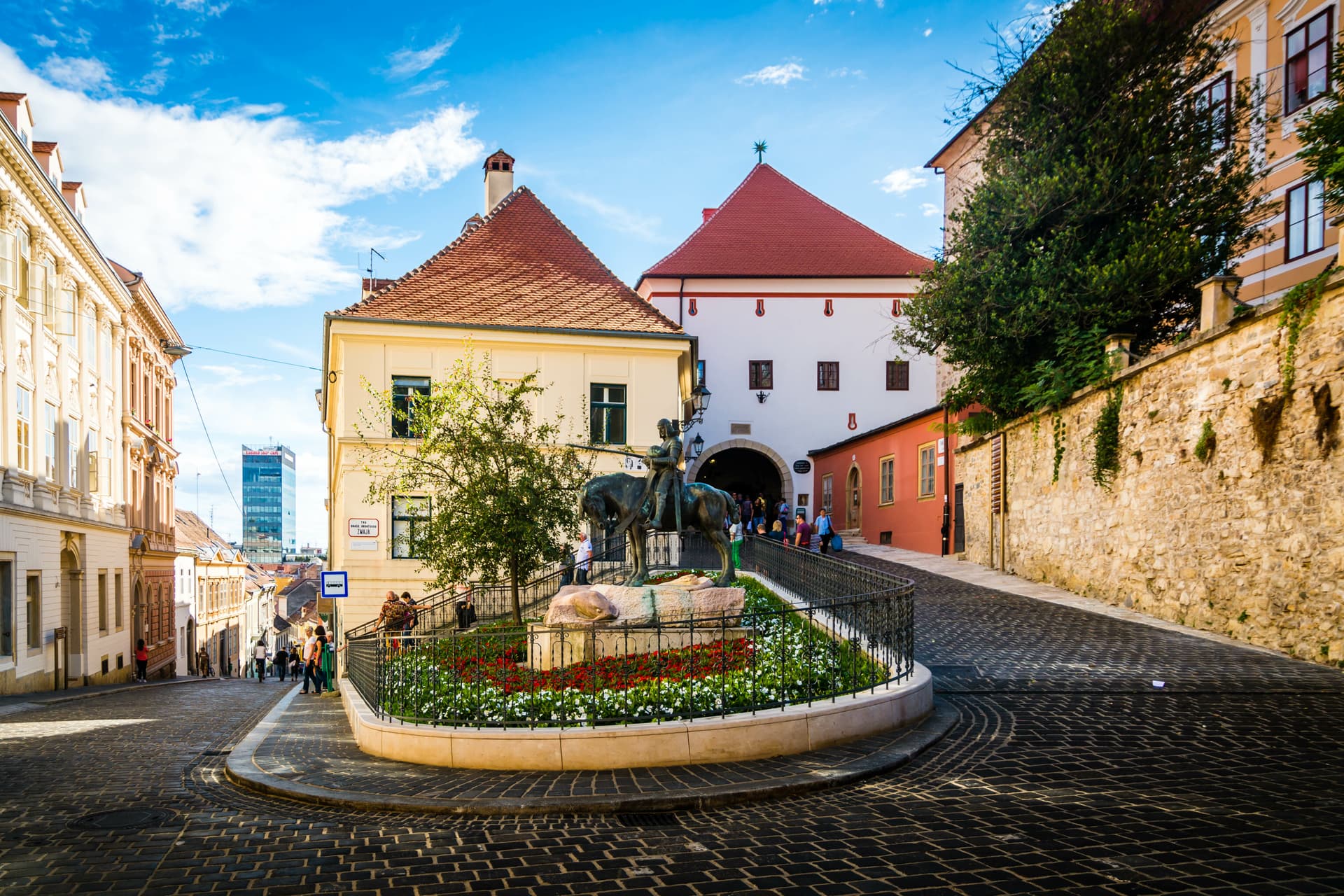 Cobblestone street leading to Lotrscak Tower entrance with equestrian statue in Zagreb.