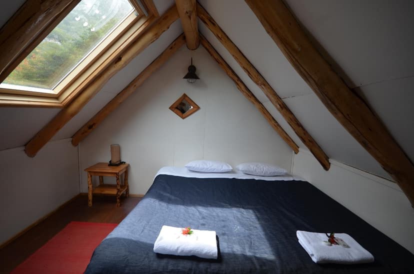 Attic cabin room with slanted wood beams, skylight, and bed with dark blue duvet